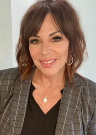 A woman wearing a black shirt and a gray jacket is smiling for the camera.