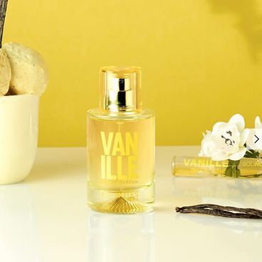 A bottle of vanille perfume is sitting on a table next to a vase of flowers.