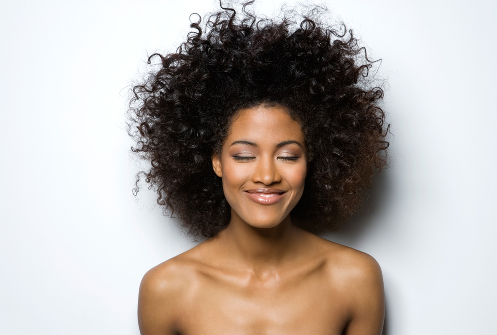 A woman with curly hair is smiling with her eyes closed.