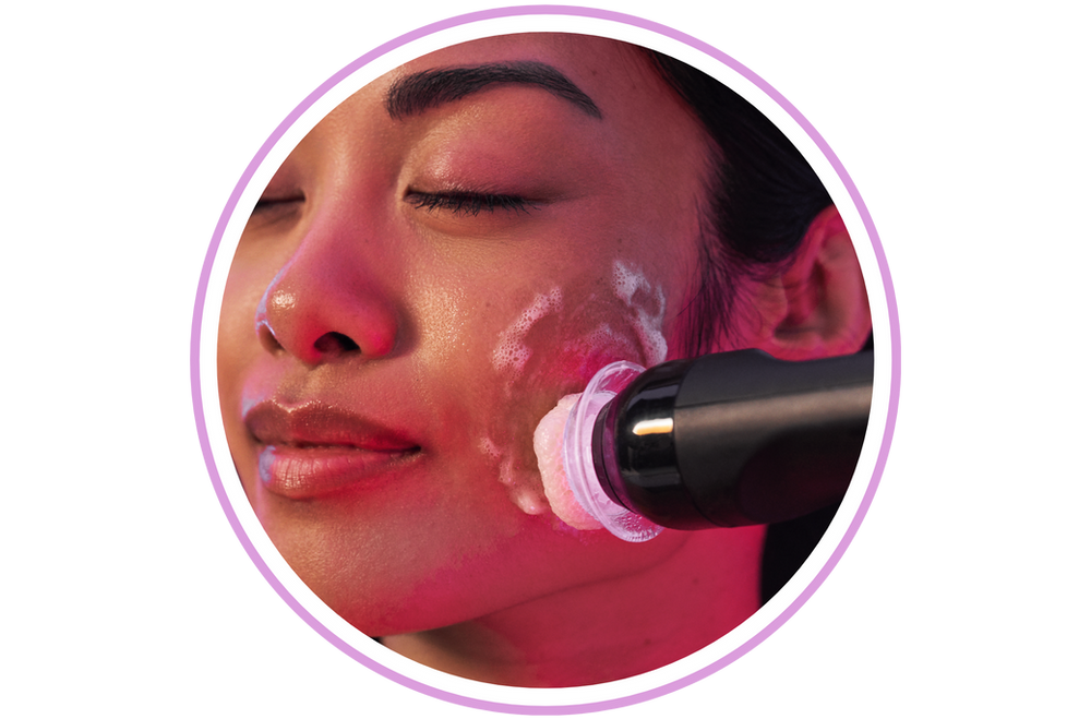 A woman is getting a facial treatment with a brush on her face.