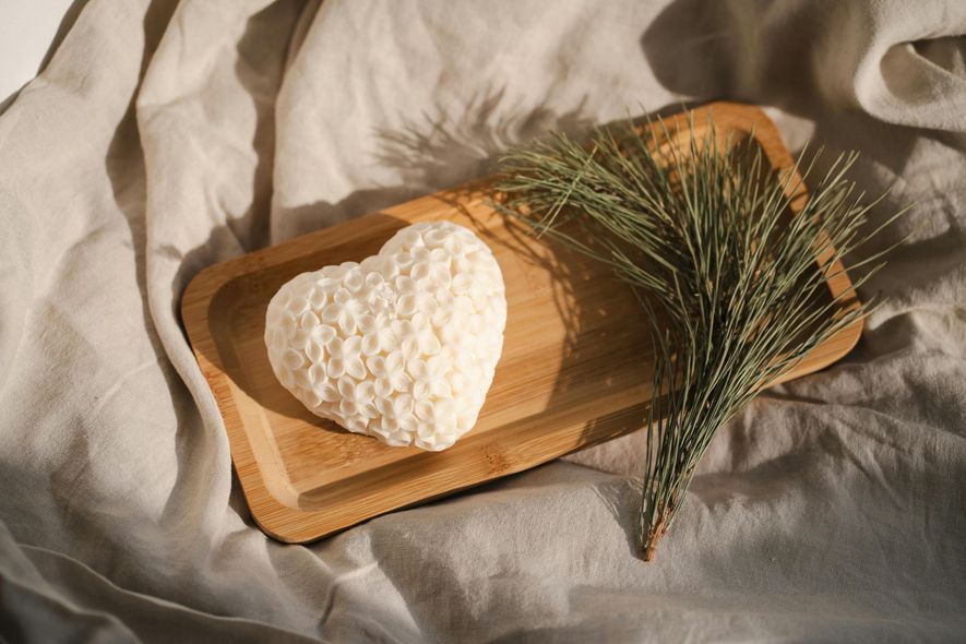 A heart shaped soap bar is sitting on a wooden tray next to a pine branch.