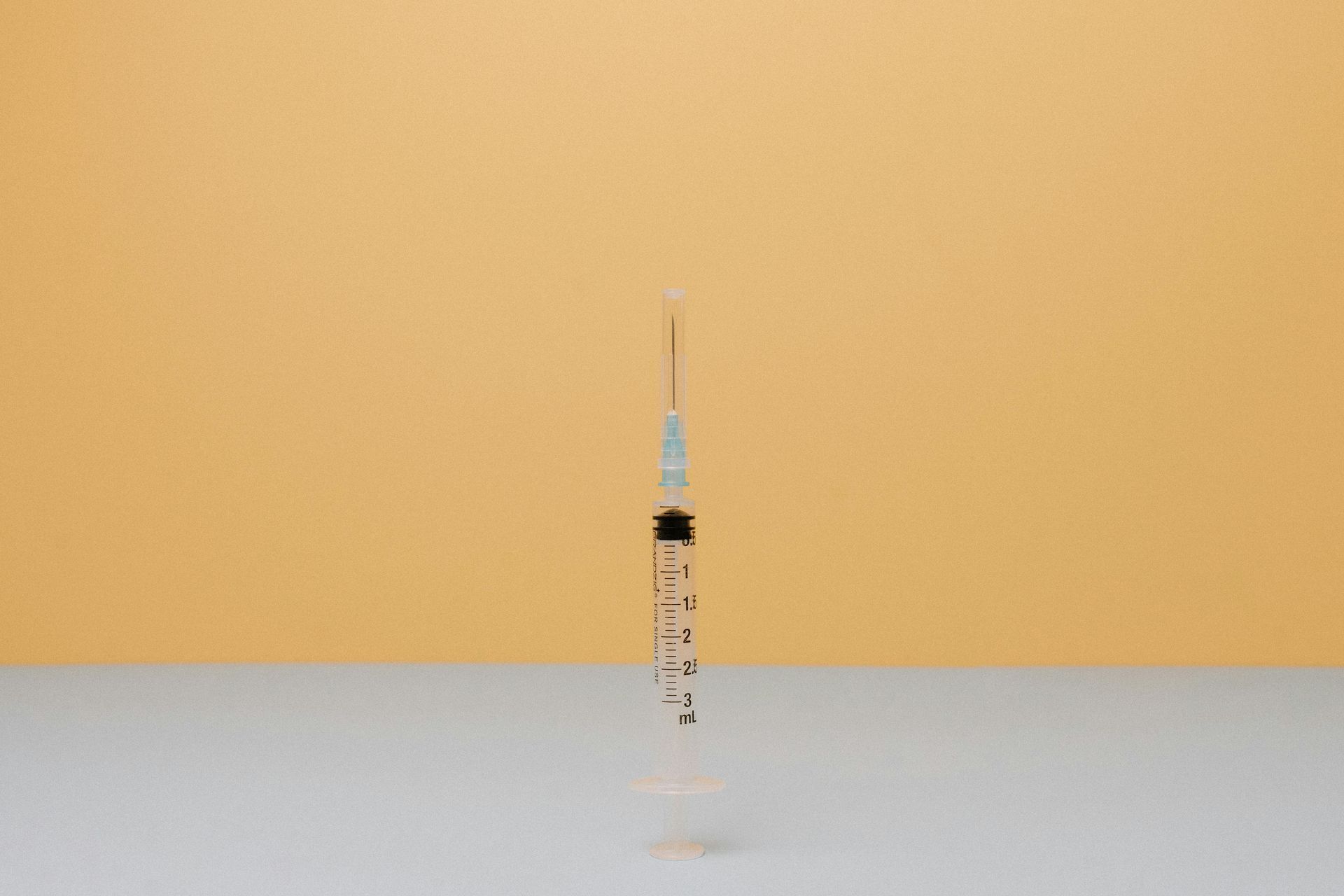 A syringe is sitting on a table with a yellow background.