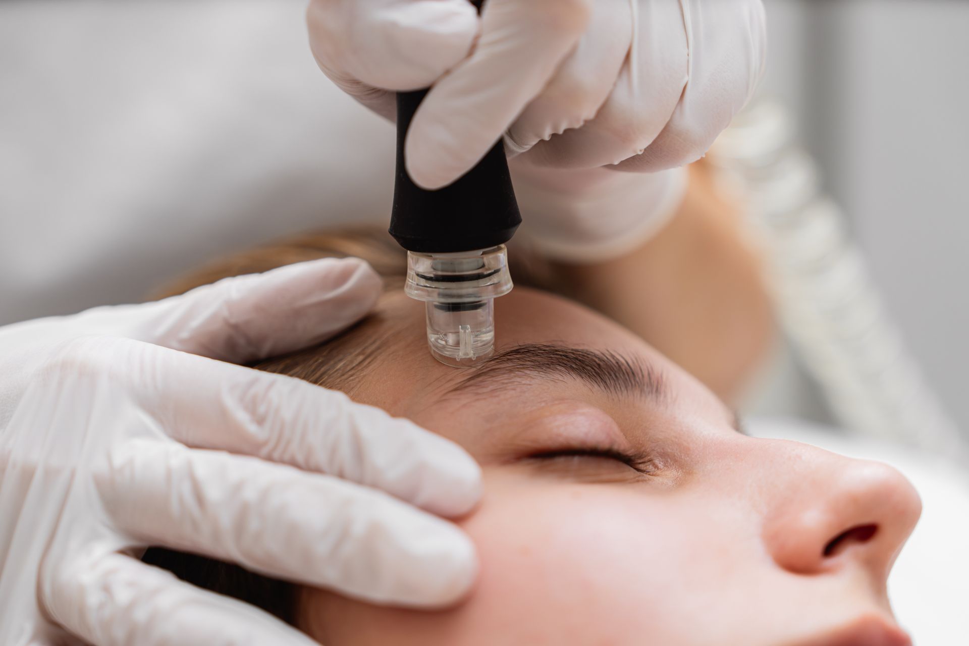 Person receiving facial treatment with gloved hands using a device on their forehead.