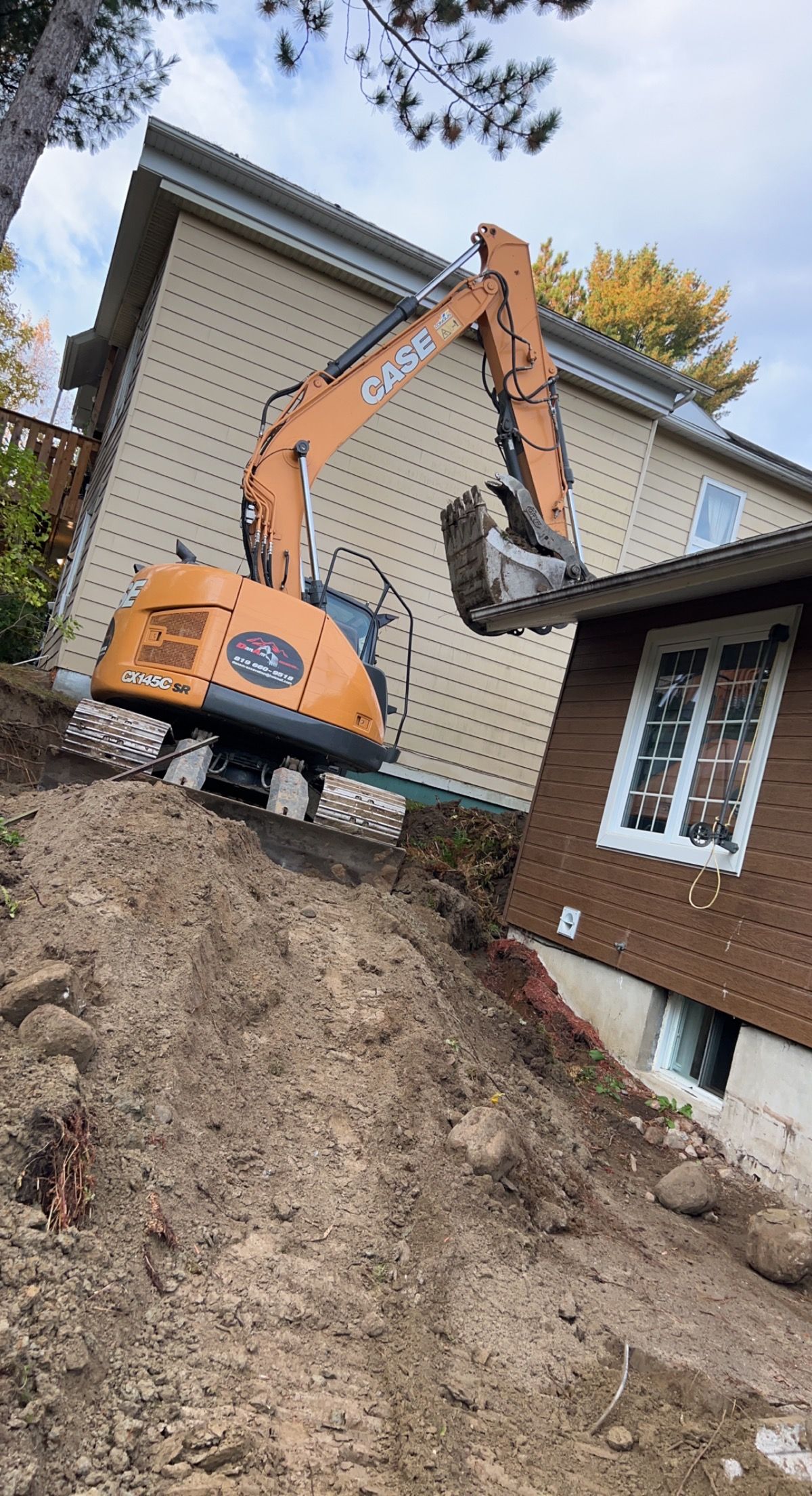 Une excavatrice creuse un trou devant une maison.