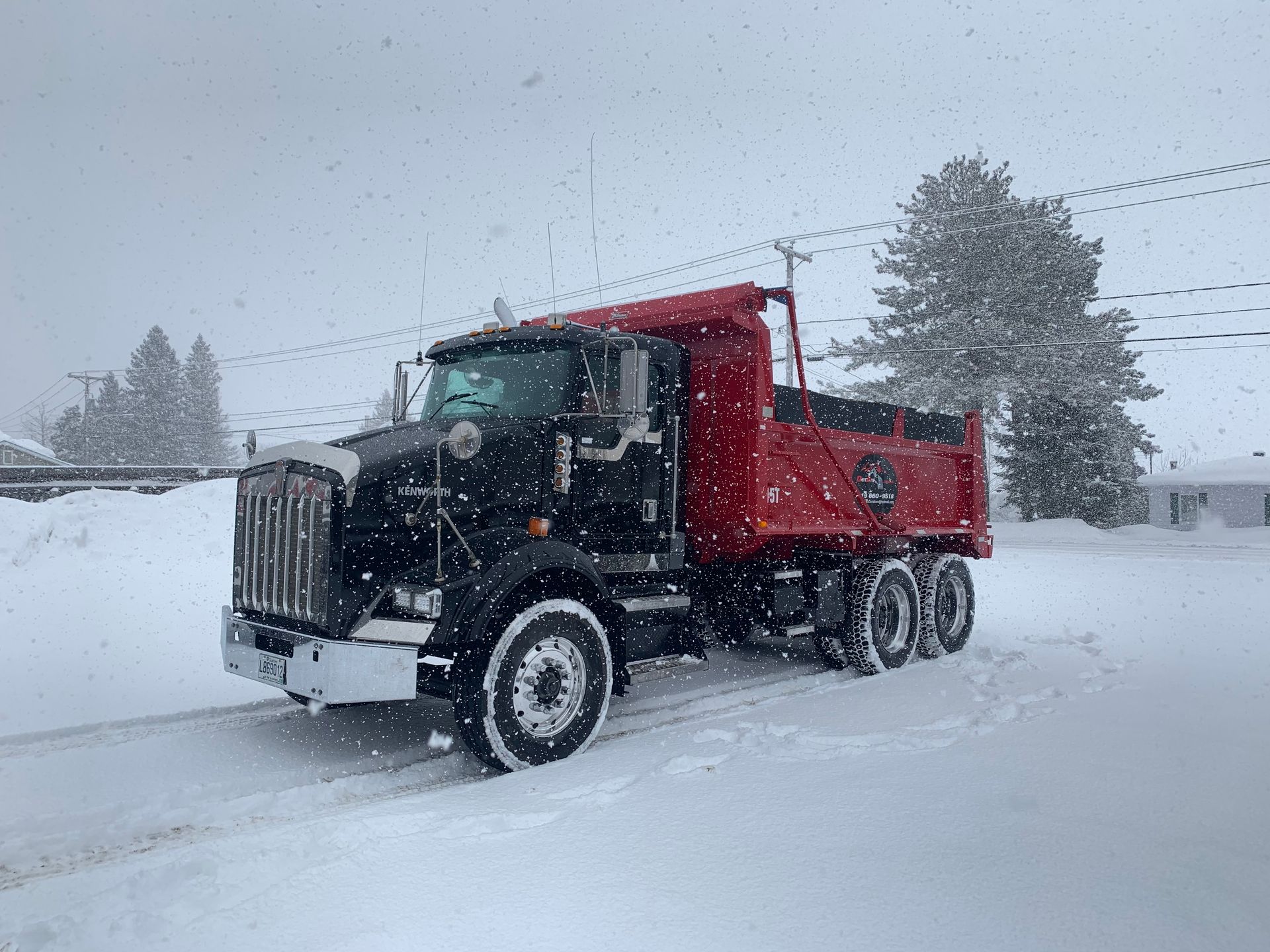 Un camion à benne rouge est garé dans la neige sur une route enneigée.