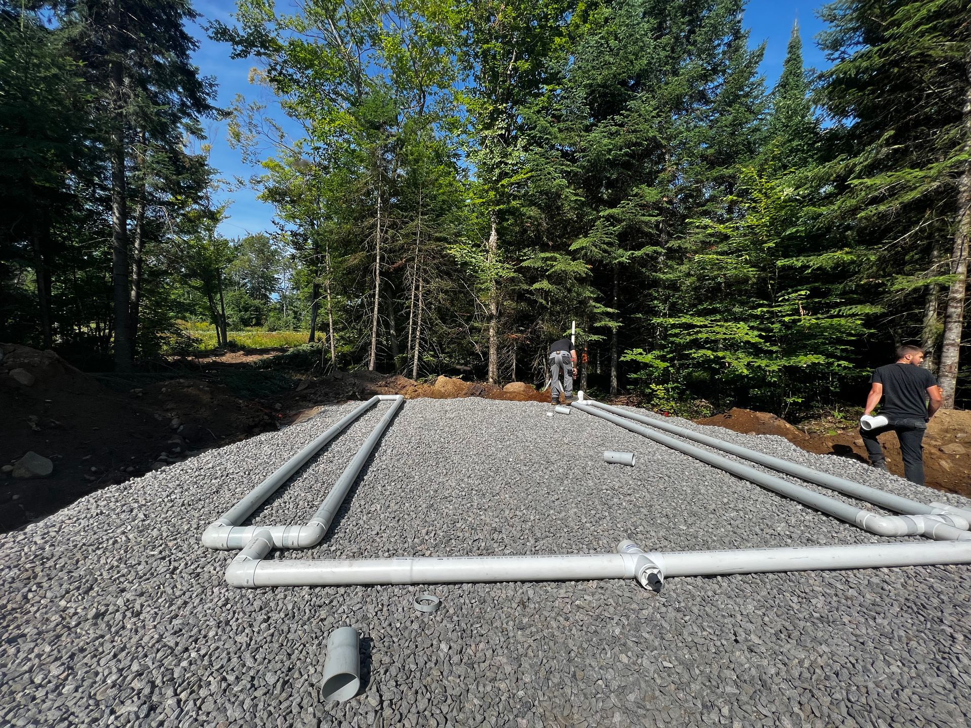 Un homme se tient à côté d’un tas de graviers et de tuyaux.
