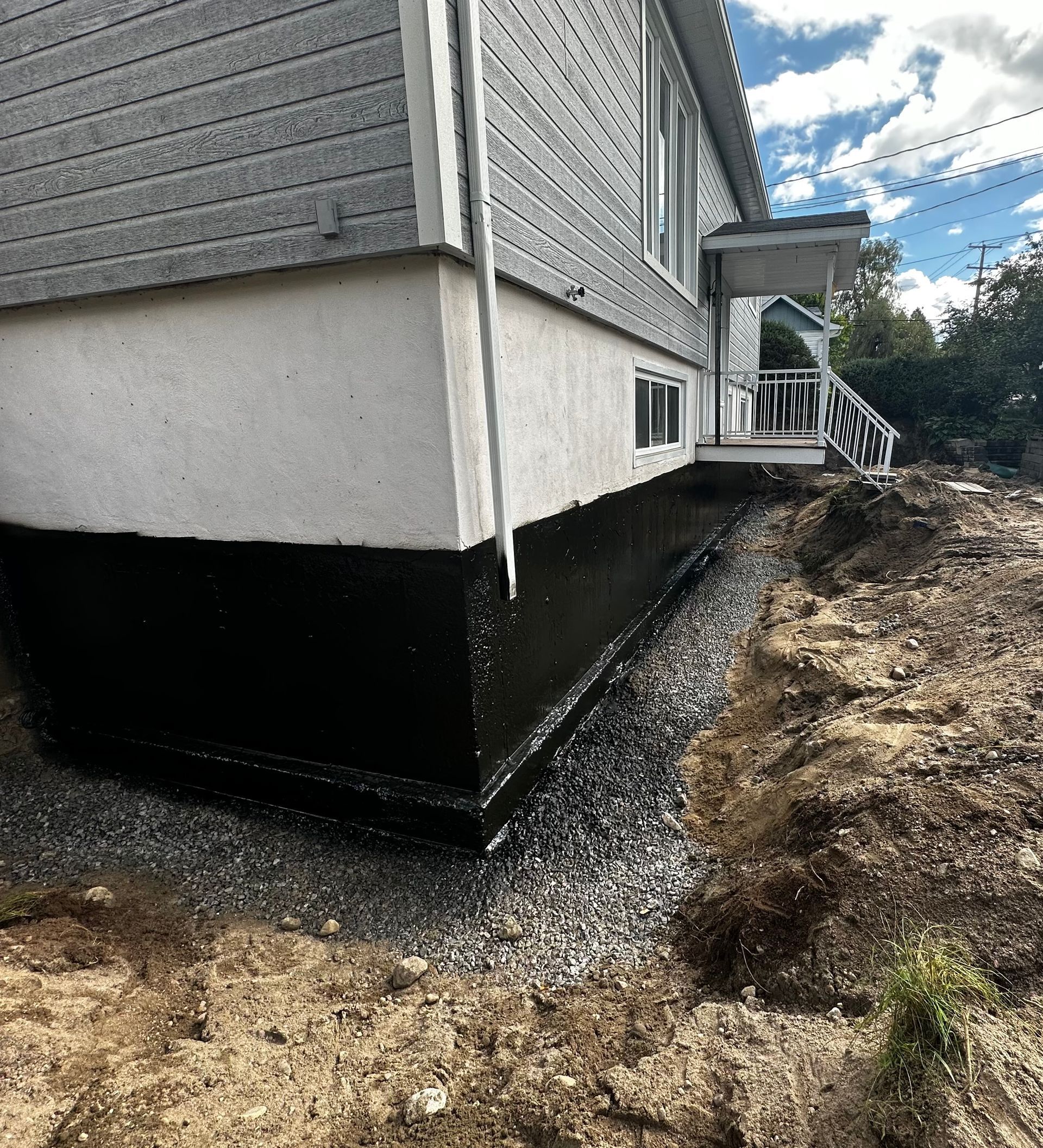 Une maison blanche avec des fondations noires se trouve au sommet d’une colline de terre.