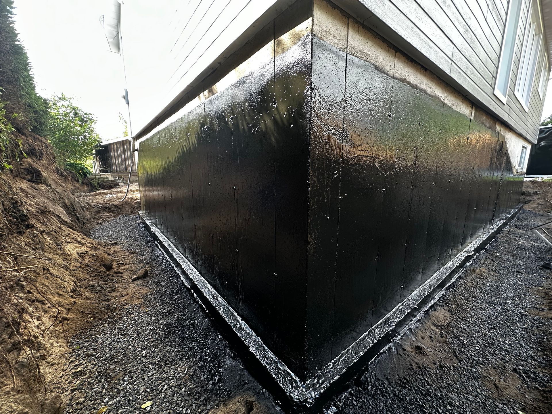 Le coin d’une maison est recouvert d’un imperméabilisant noir.