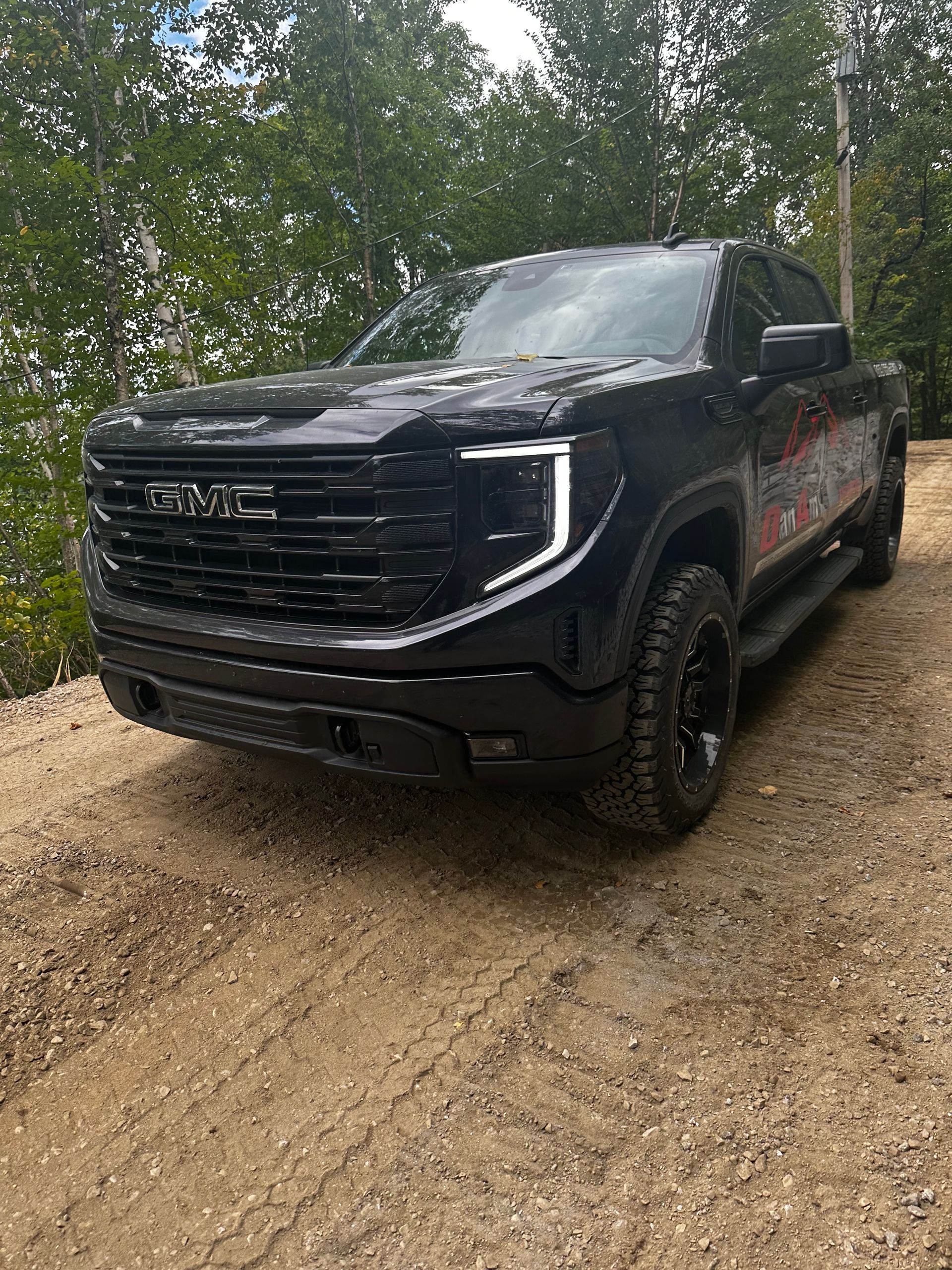 Un camion GMC noir est garé sur un chemin de terre.