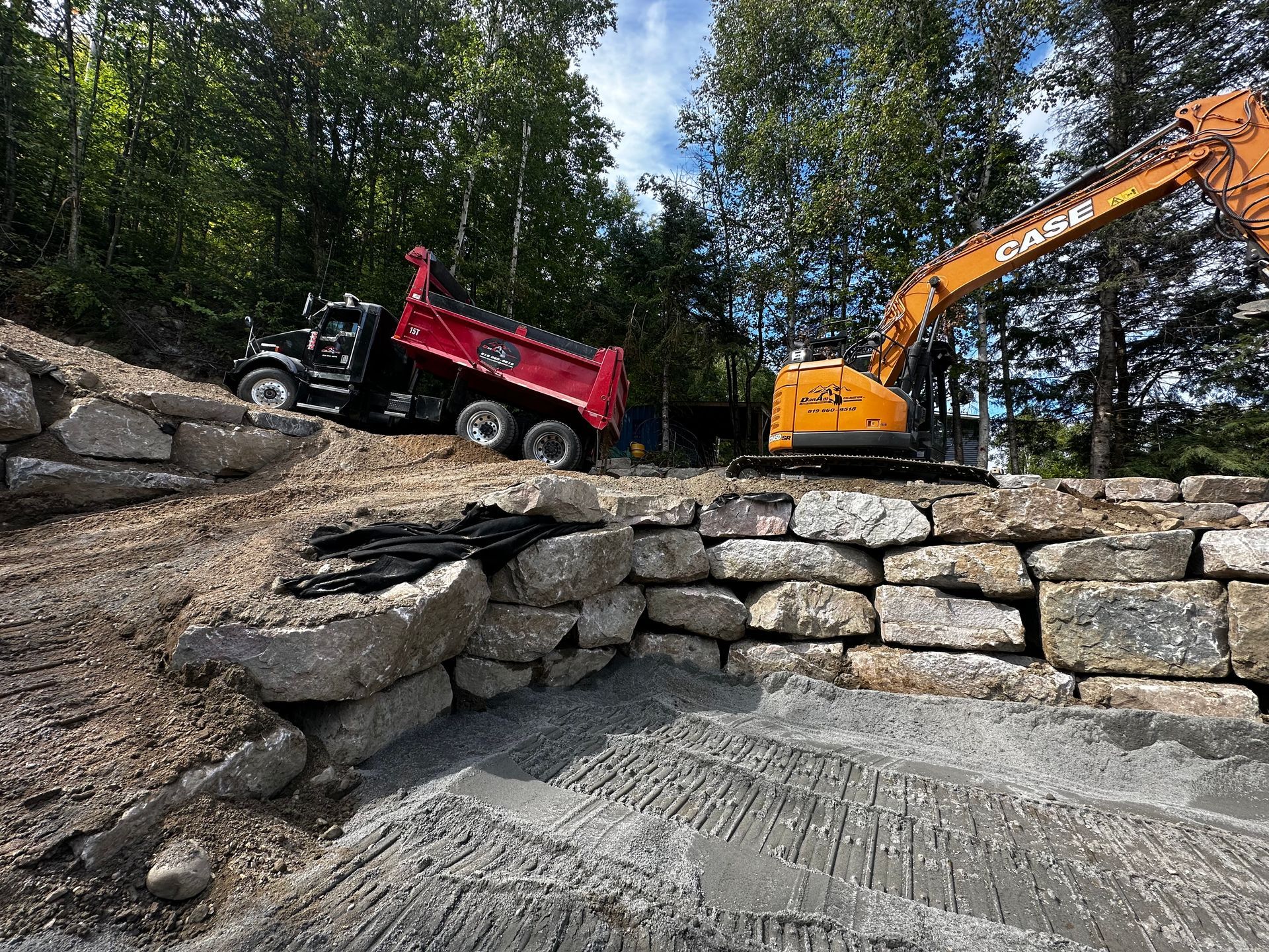Un camion-benne est posé au sommet d’une paroi rocheuse à côté d’une excavatrice.