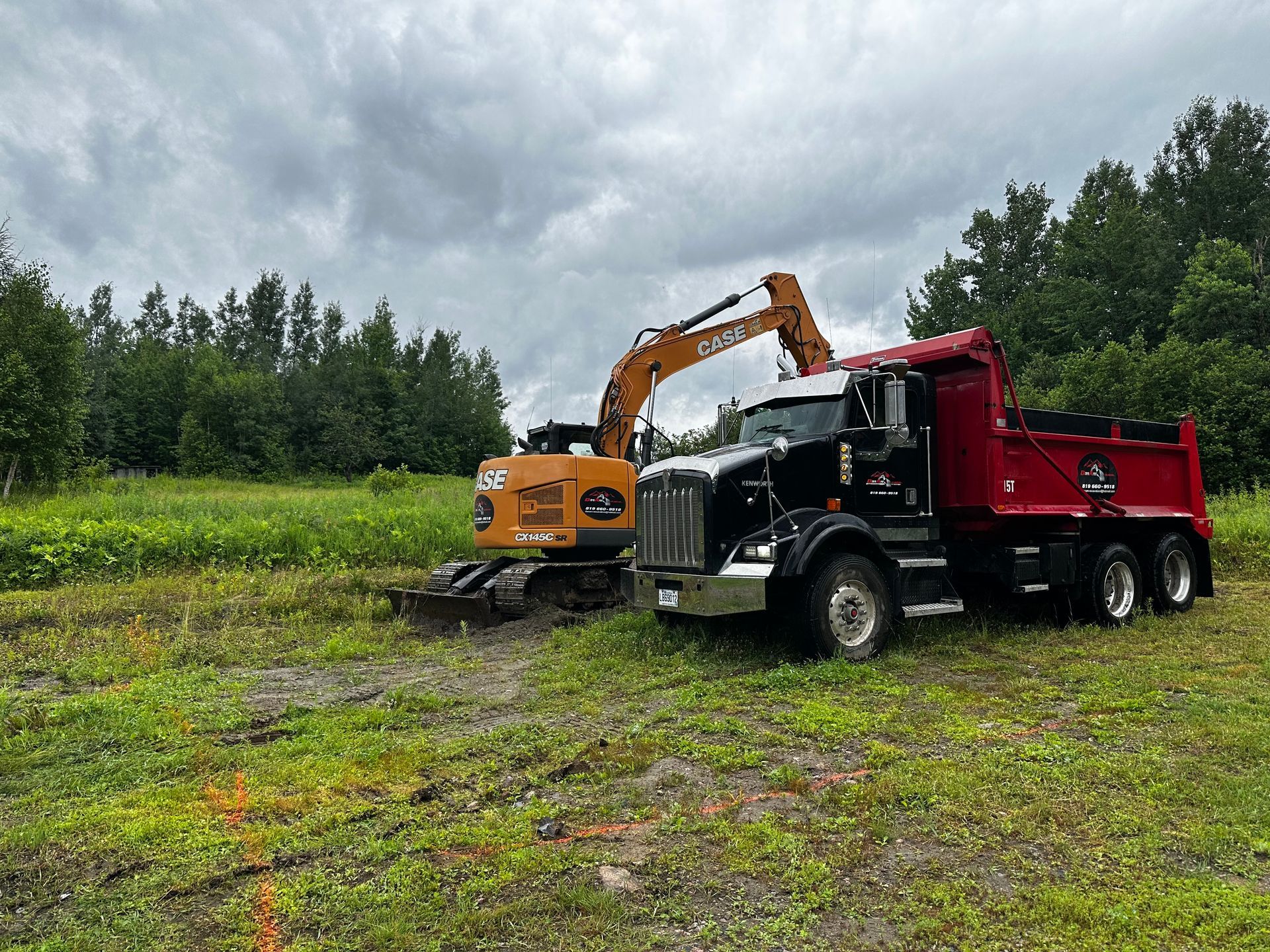Un camion-benne et une excavatrice sont garés dans un champ herbeux.