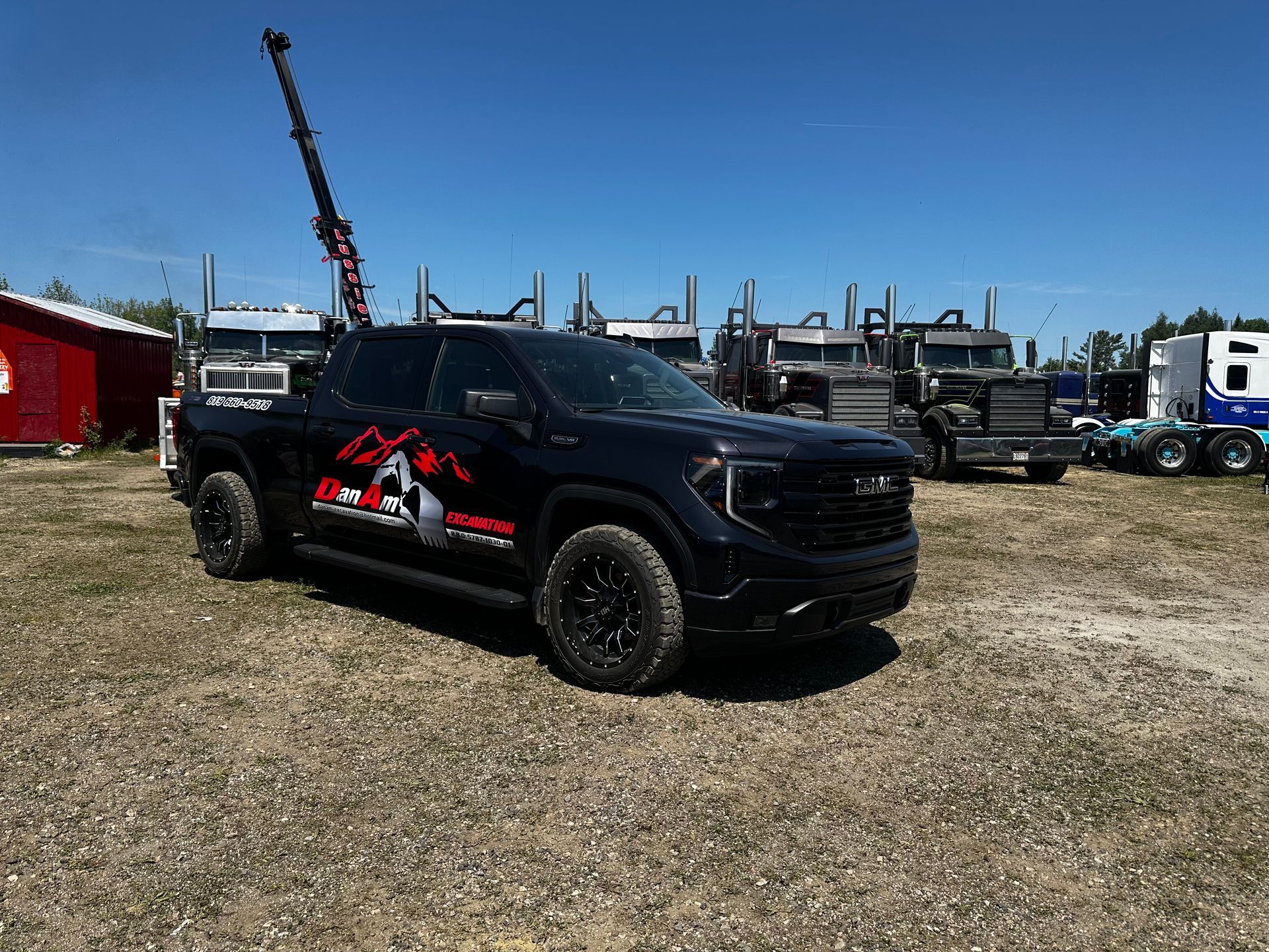Un camion noir surmonté d’une grue est garé dans un terrain de gravier.