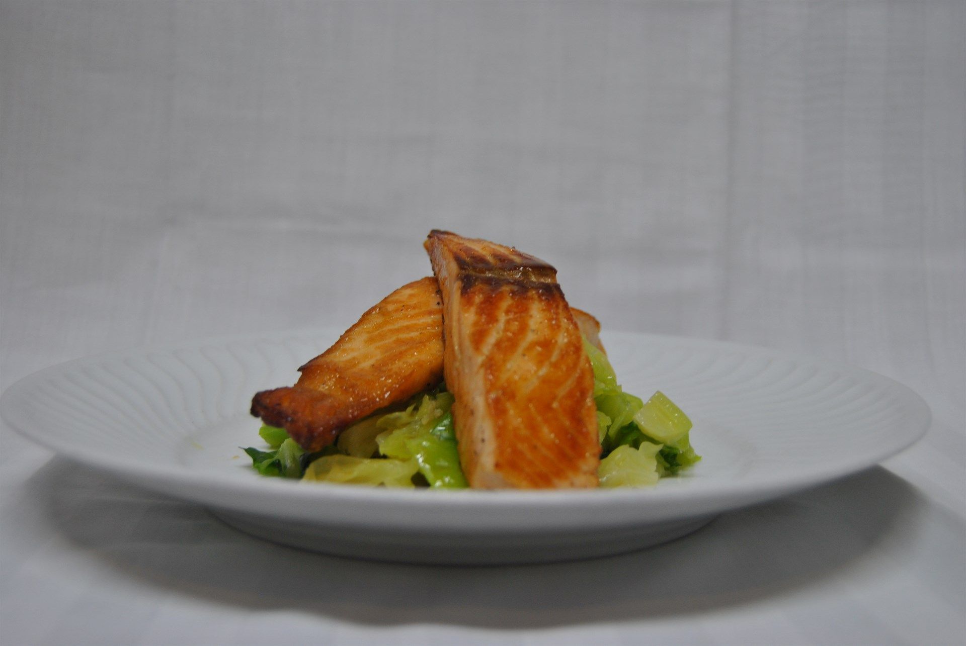 Um prato branco coberto com um pedaço de salmão e vegetais