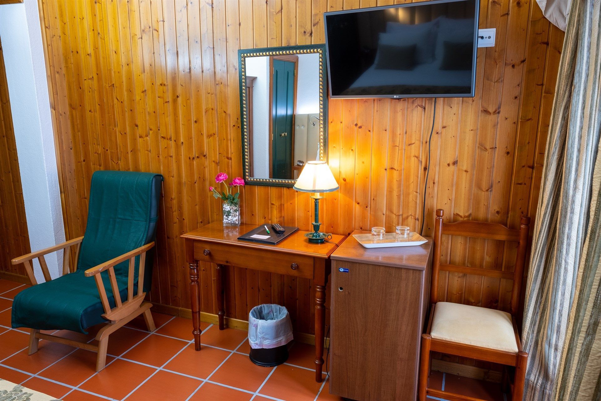 Um quarto de hotel com uma mesa, cadeira, televisão e espelho.