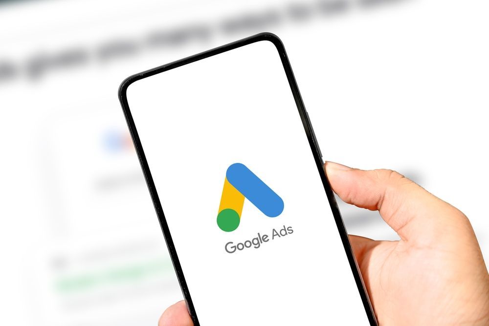 Hand holding a smartphone displaying the Google Ads logo.