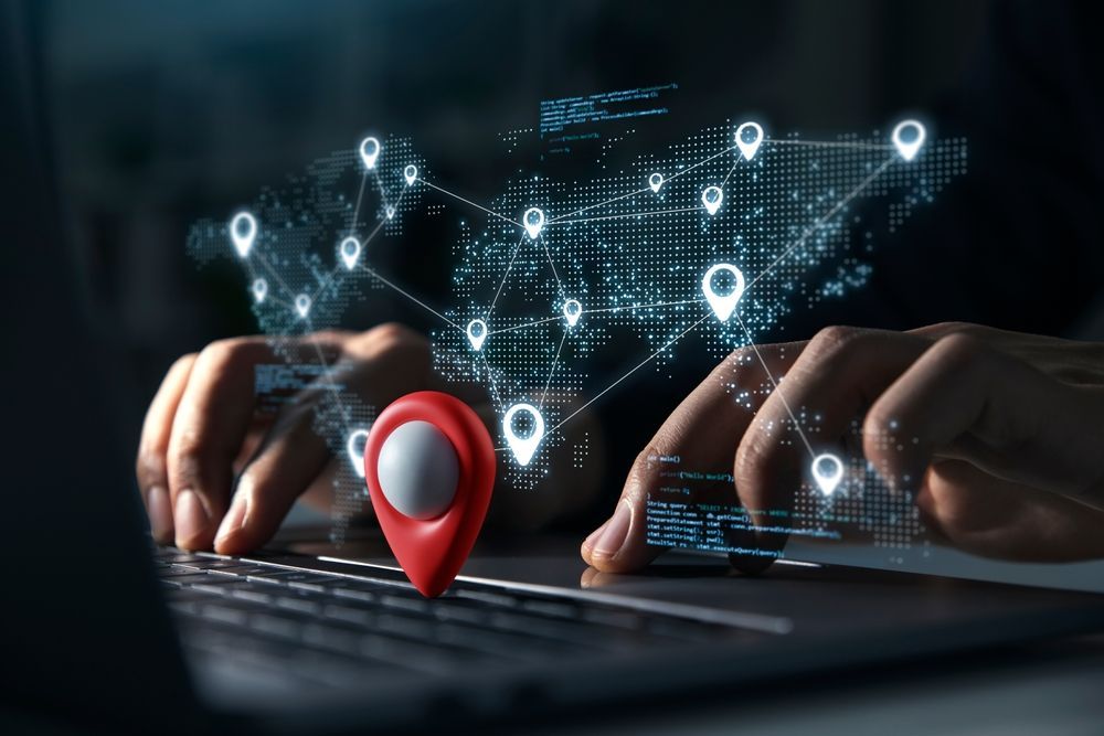 Hands typing on laptop with digital map and location markers overlaid.