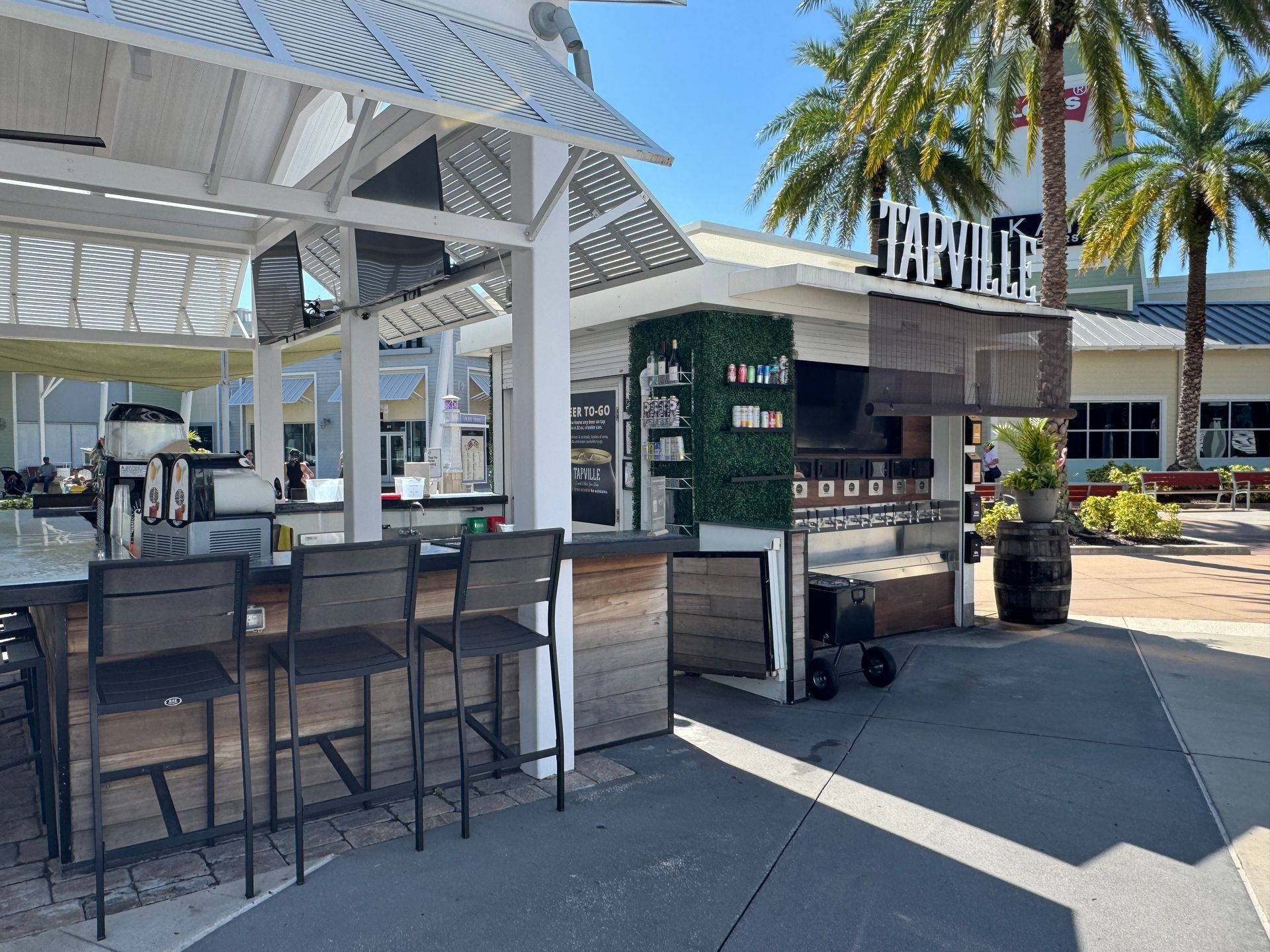 A restaurant with a bar and stools in front of a palm tree.