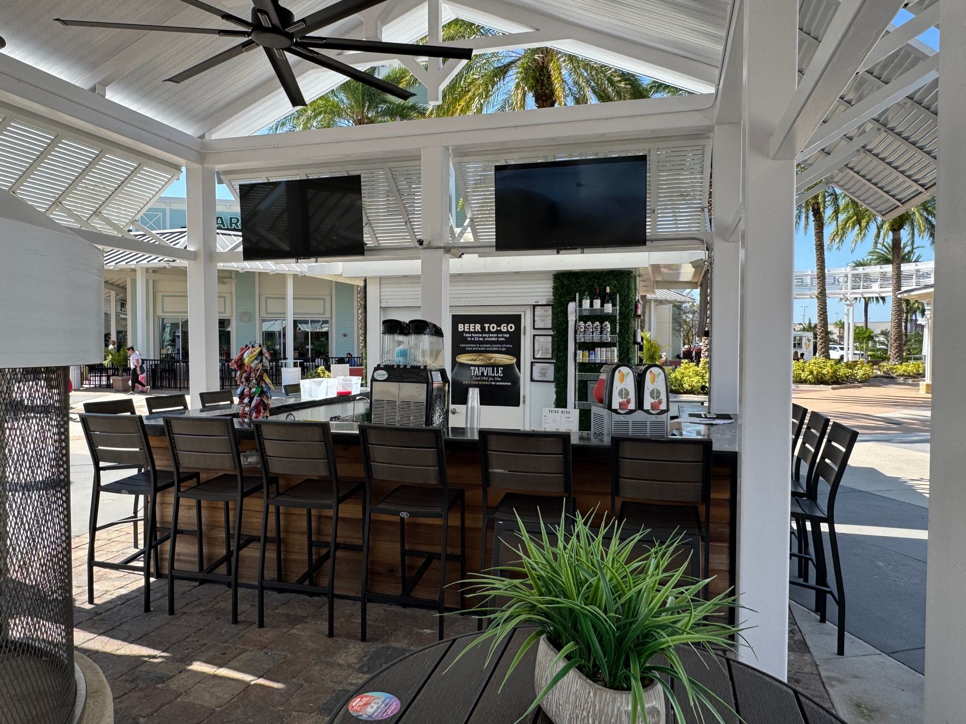 A large outdoor bar with a ceiling fan and televisions.