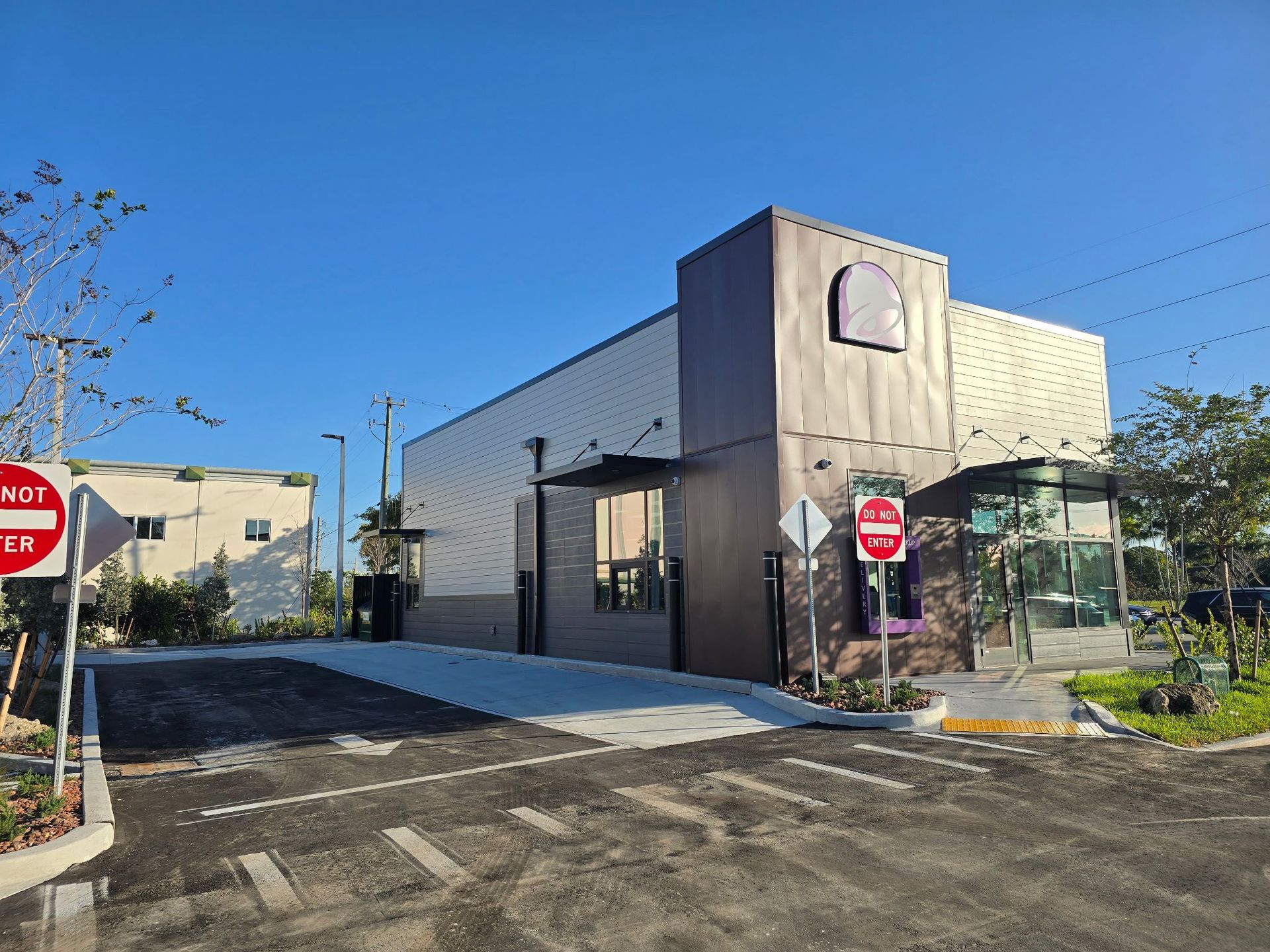 Exterior view of a Taco Bell restaurant with a drive-thru, gray and purple color scheme, and “Do Not Enter” signs.