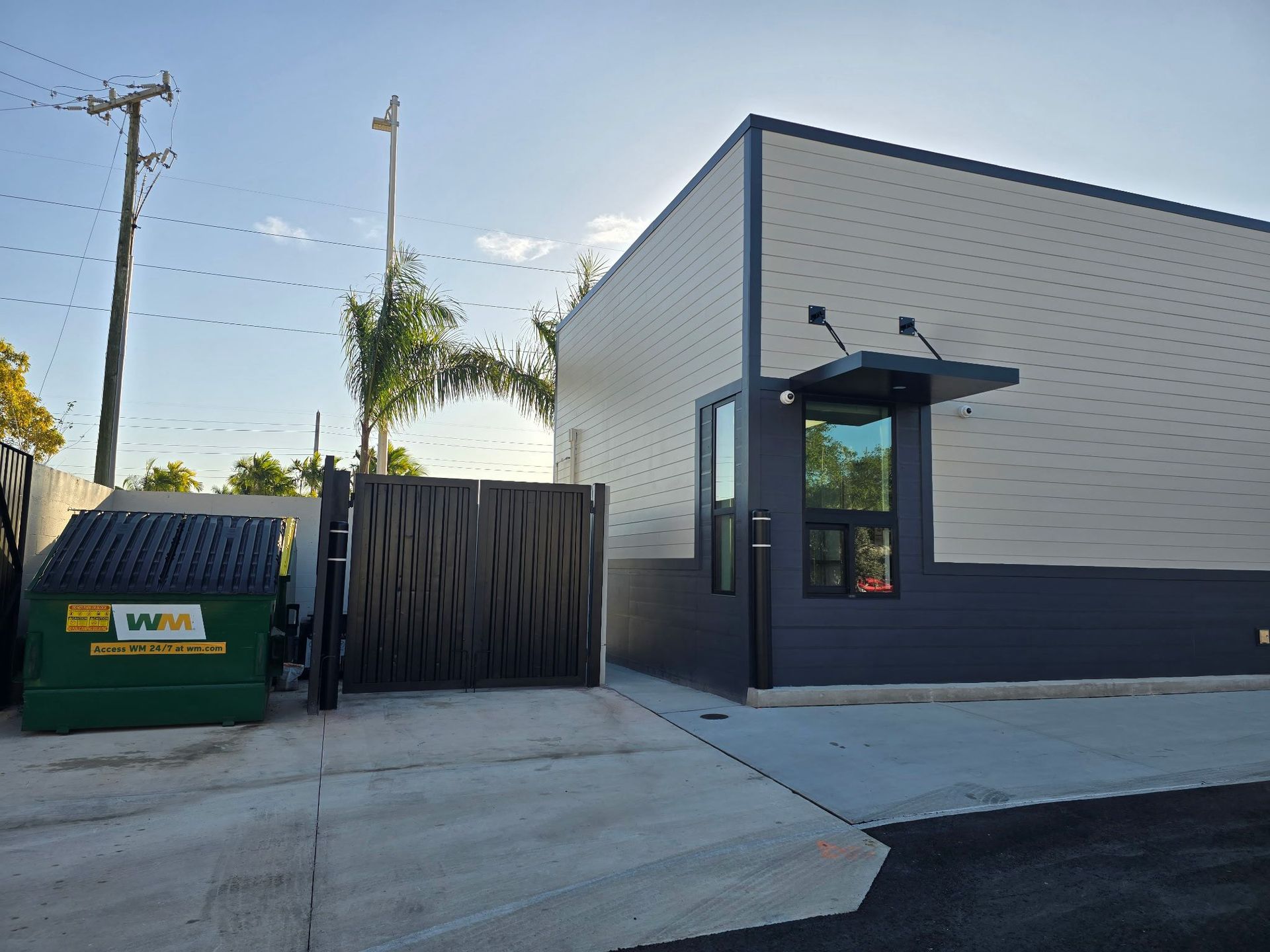 Exterior of a modern building with a trash receptacle. Light-colored siding, dark gray accents, and a small awning.