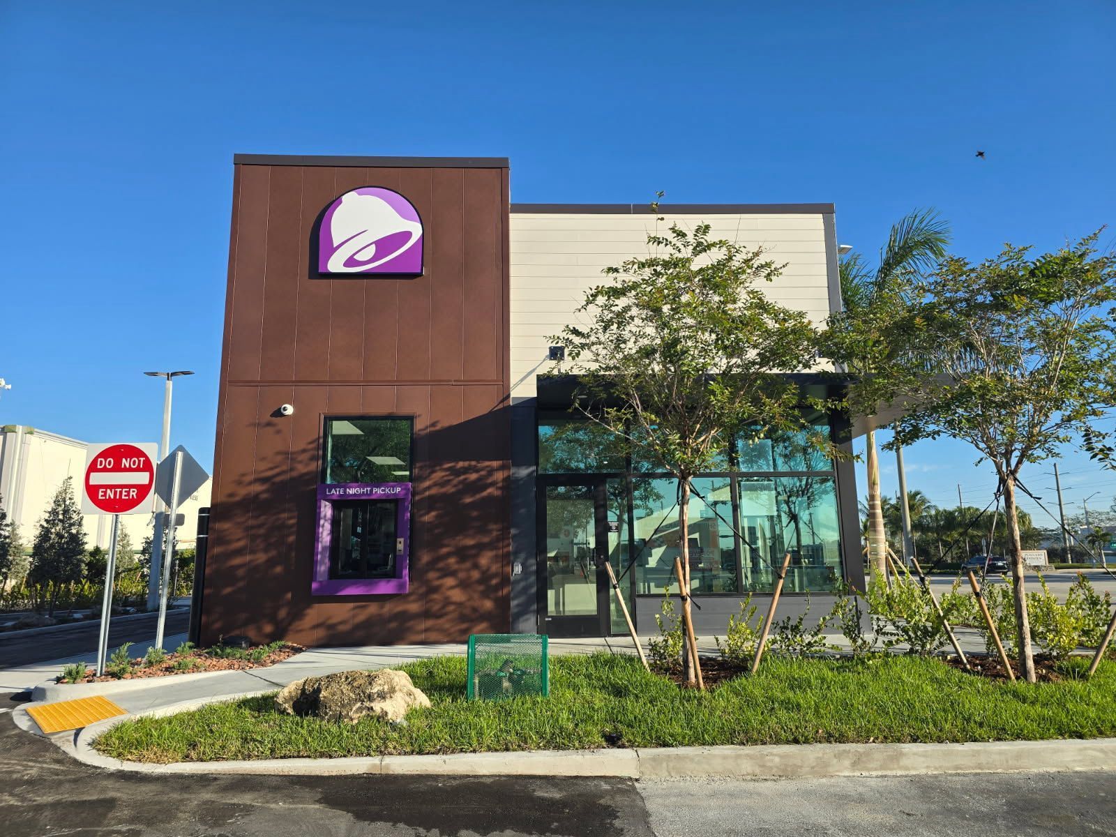 Taco Bell restaurant with brown and beige facade, purple logo, glass front, and landscaping.