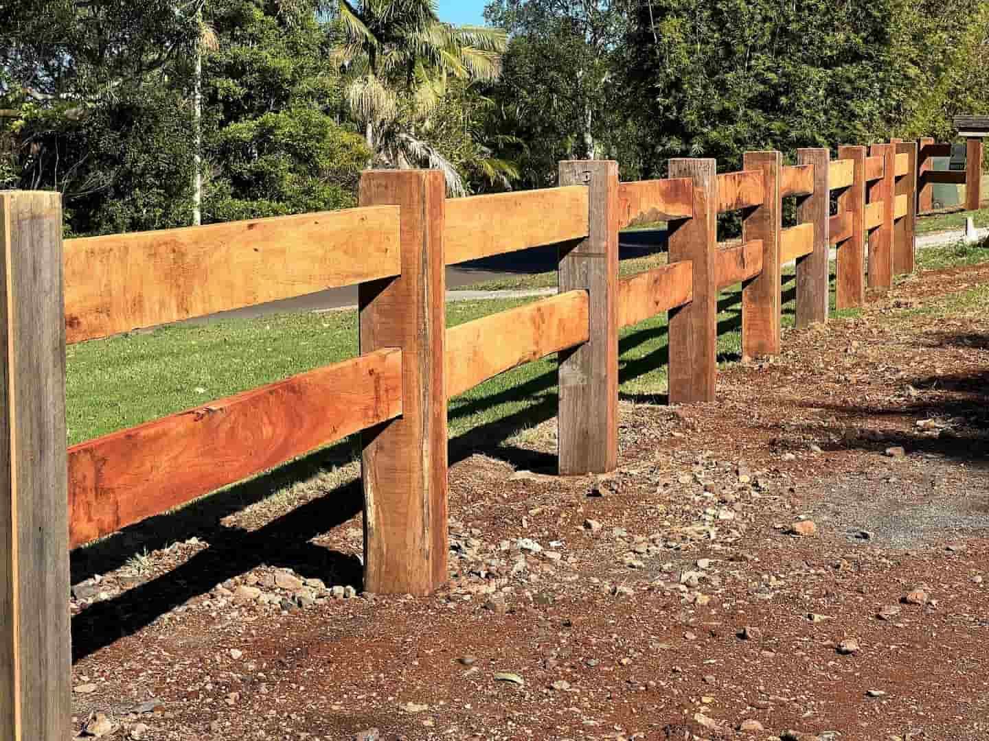 A Wooden Fence Surrounds a Grassy Field With Trees in the Background — B & B Timbers Ballina In West Ballina, NSW