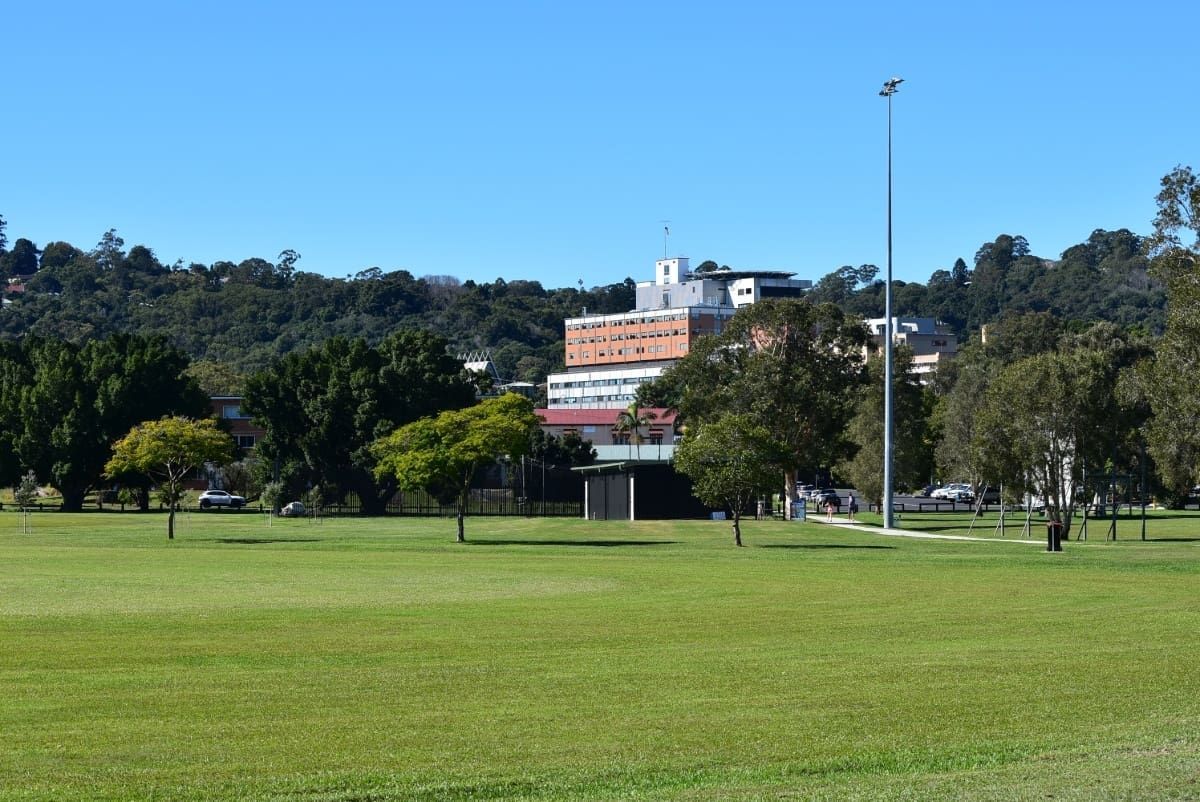 A Lush Green Field With Trees and a Building in the Background — B & B Timbers Ballina In Lismore, NSW