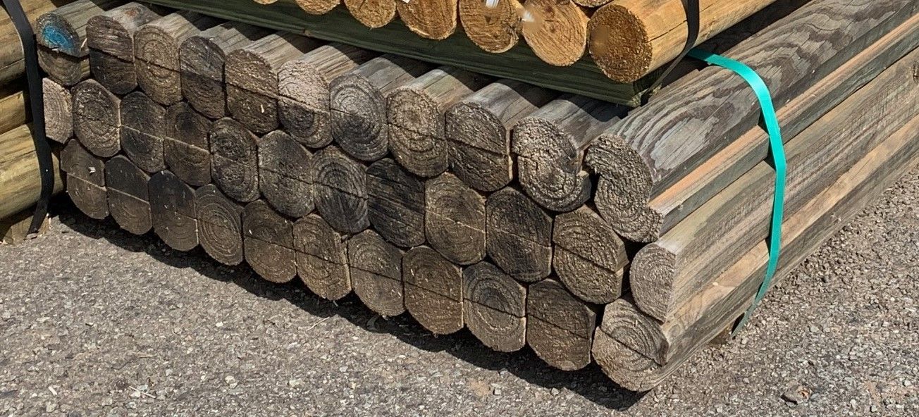 Stacked cut logs bundled with a turquoise strap on gravel. — B & B Timbers Ballina In West Ballina, NSW