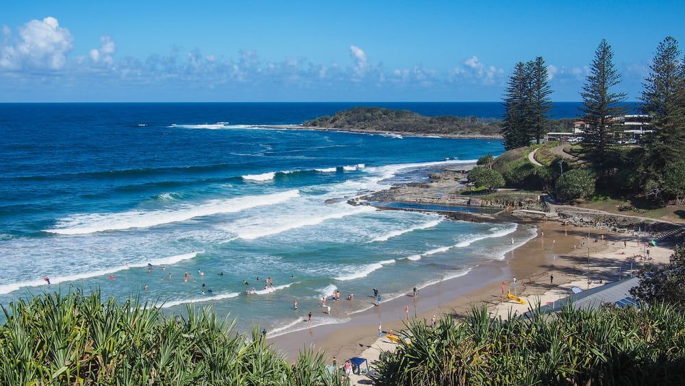 A Beach With a Lot of People on It and Waves Crashing on the Shore — B & B Timbers Ballina In Yamba, NSW