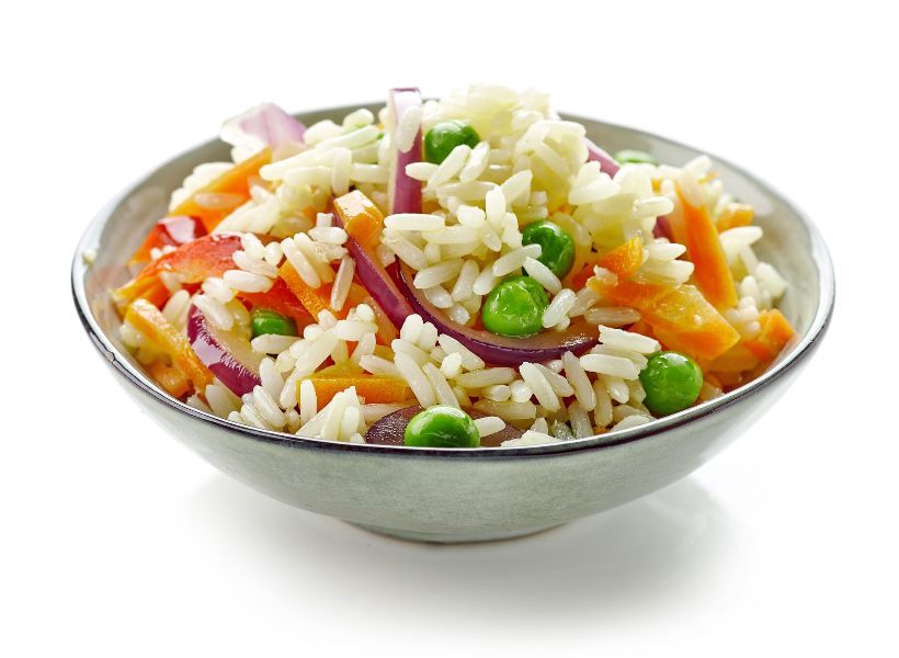 A bowl of rice with carrots , peas and onions on a white background.