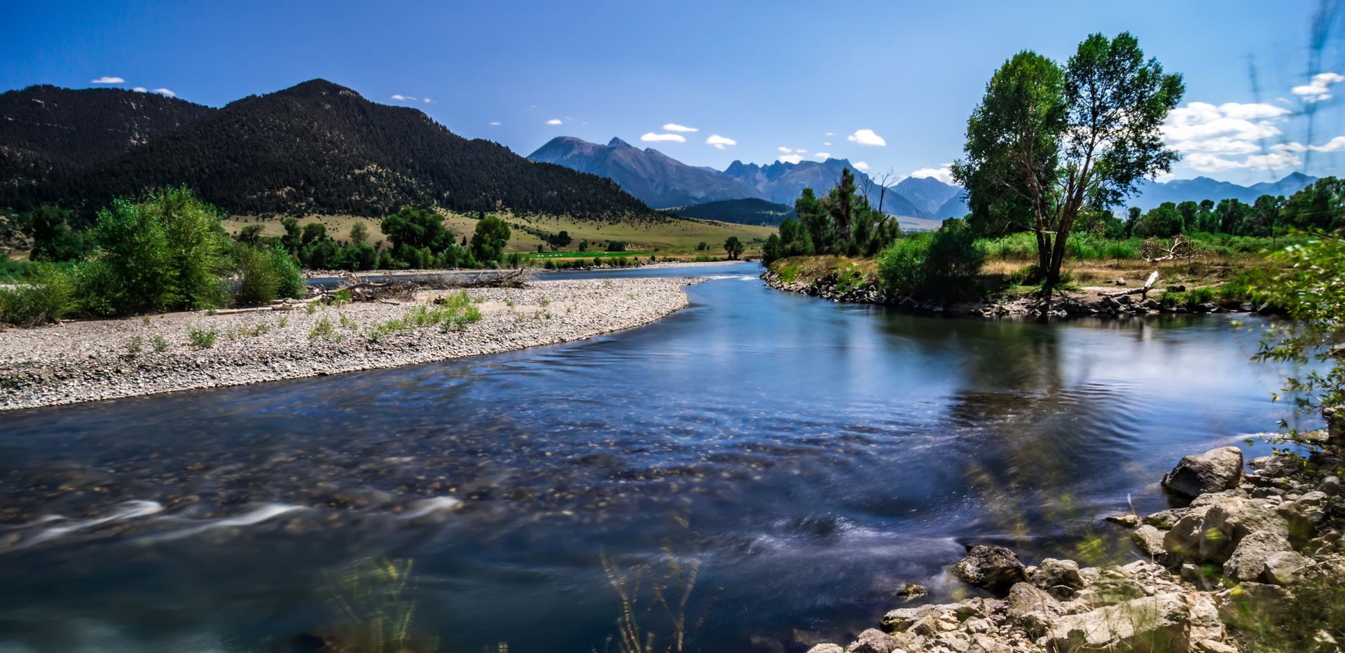 A river flowing through a lush green field with mountains in the background.