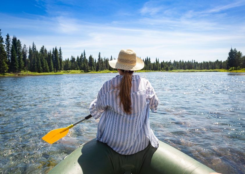 A woman in a straw hat is rowing a boat on a lake.