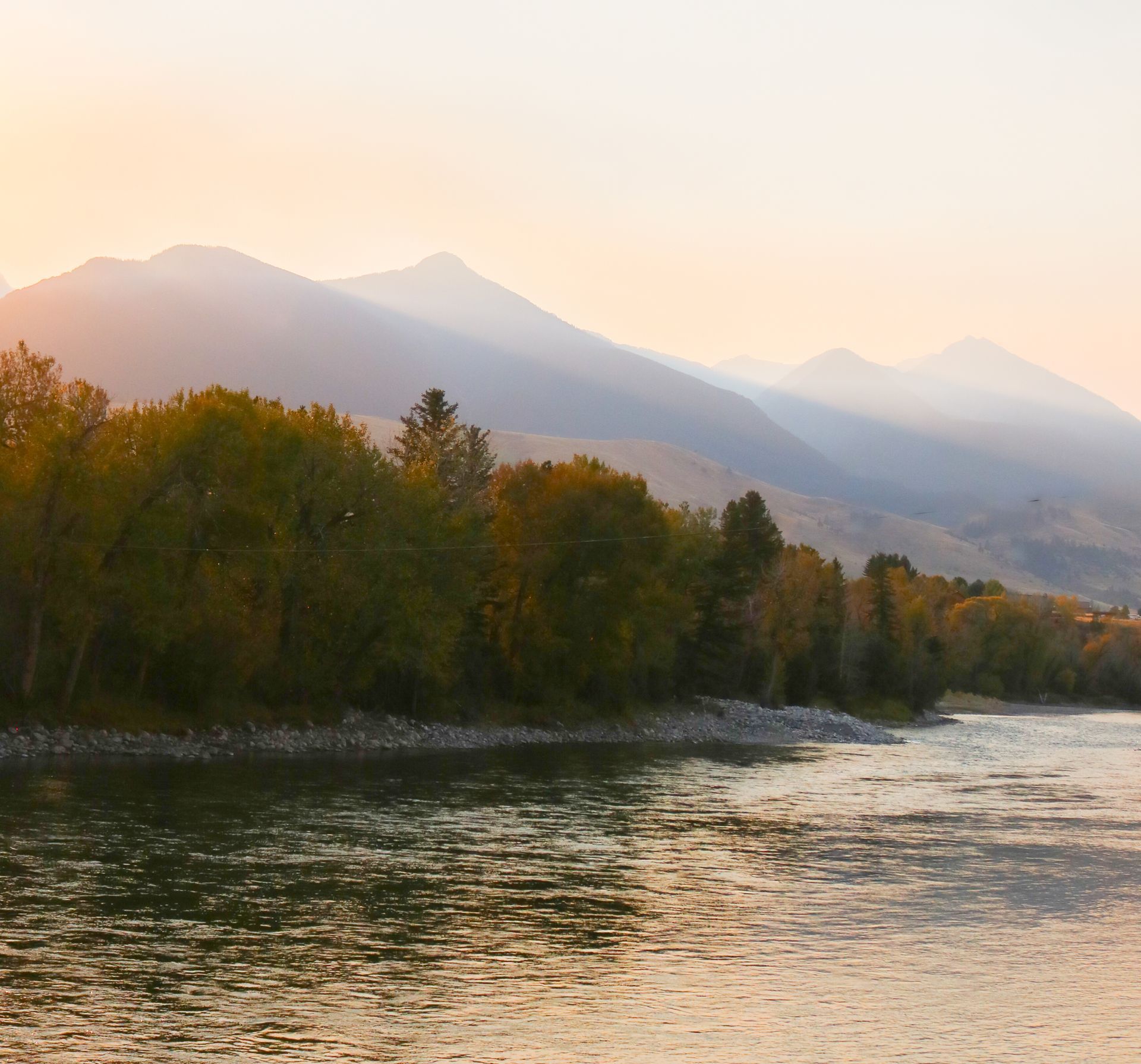 A river with mountains in the background and trees on the shore