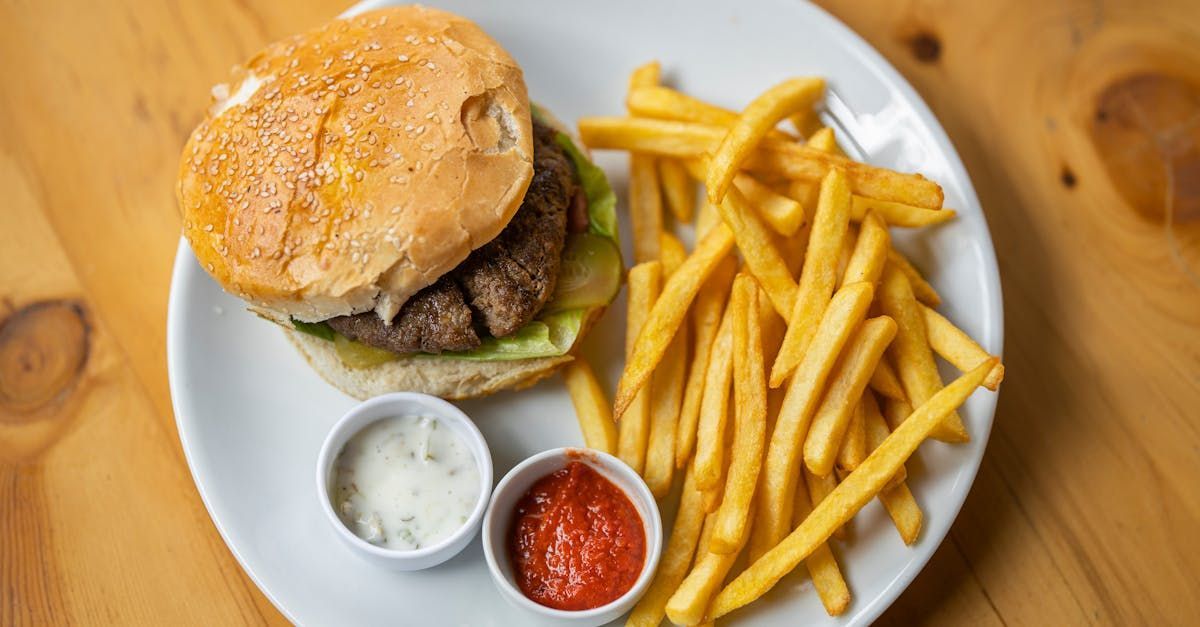 A white plate topped with a hamburger and french fries on a wooden table.