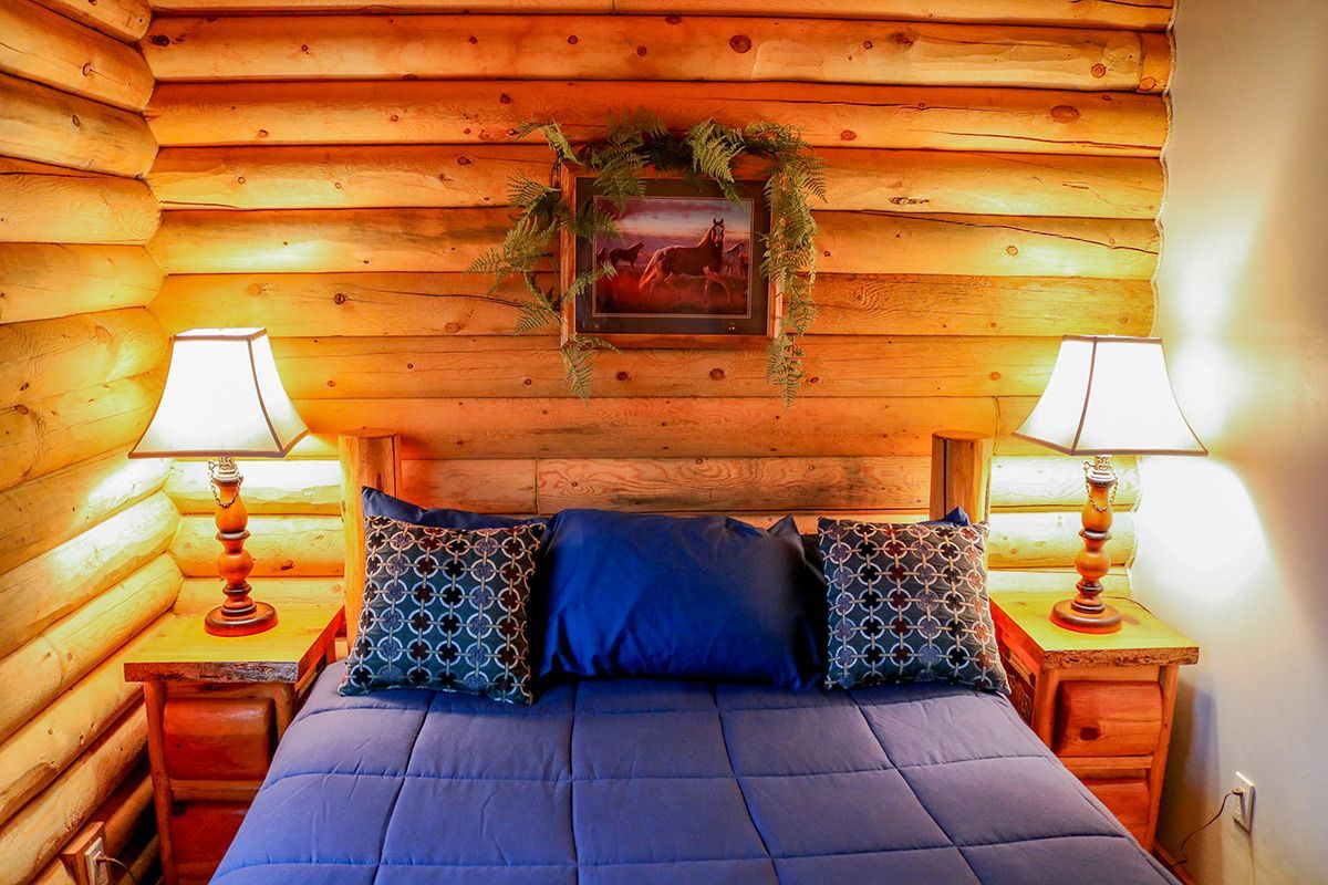 A bedroom in a log cabin with a bed and two lamps.