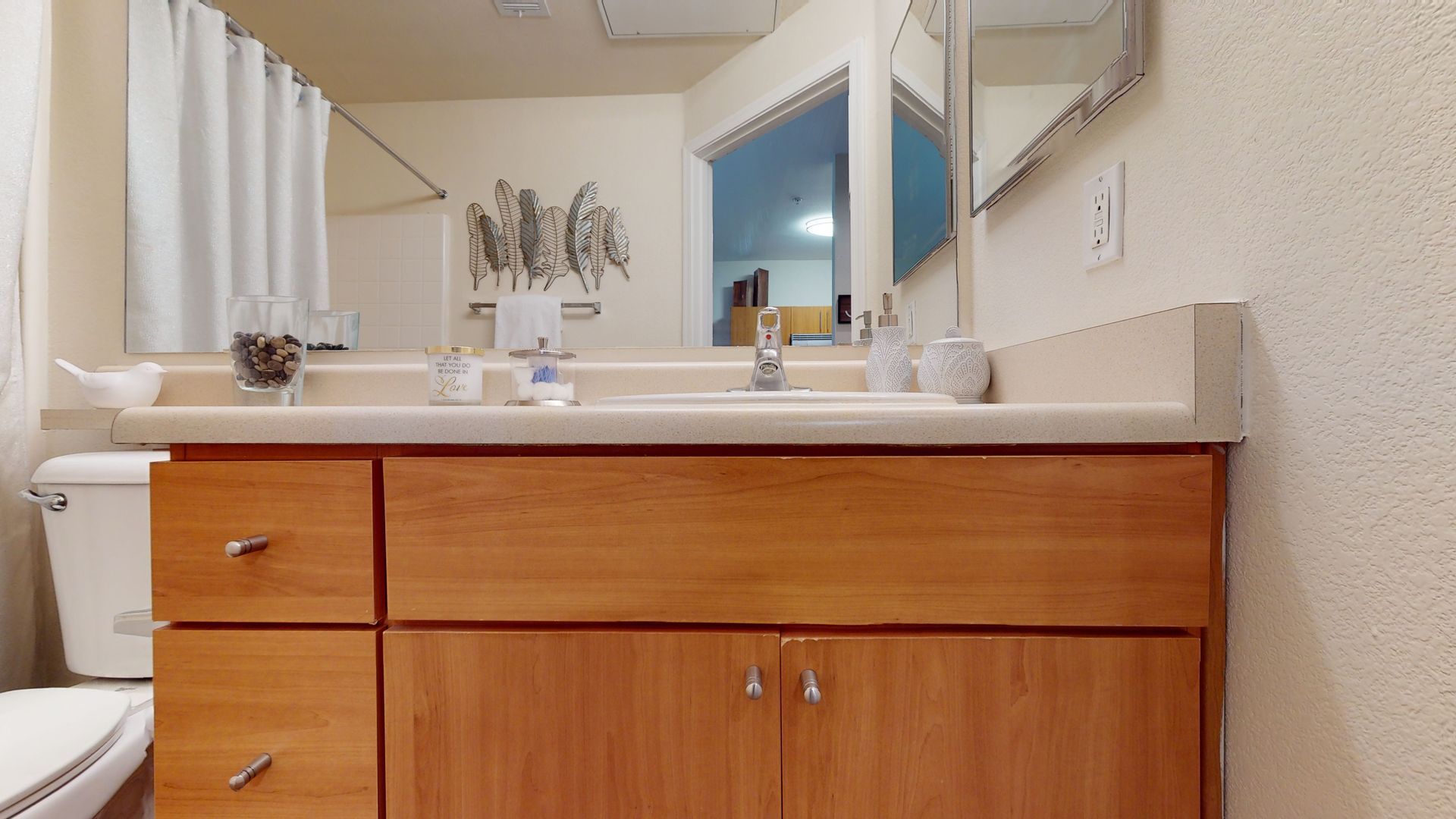 A bathroom with a sink , toilet , mirror and wooden cabinets.