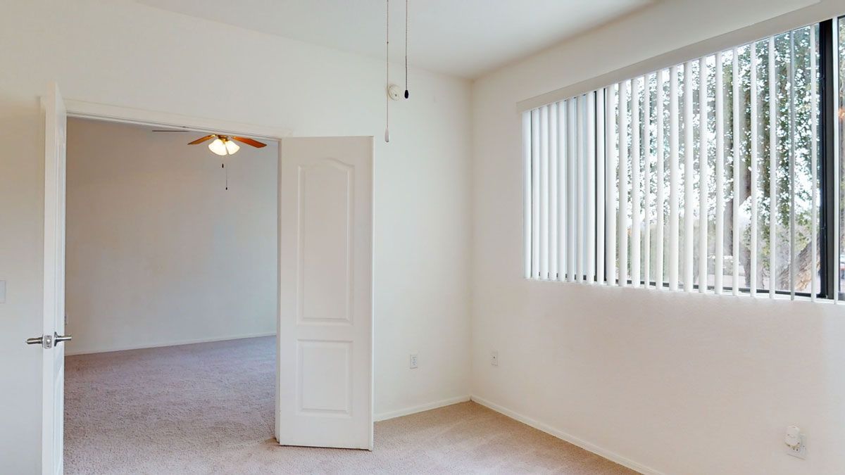 An empty room with a ceiling fan and a window with blinds.