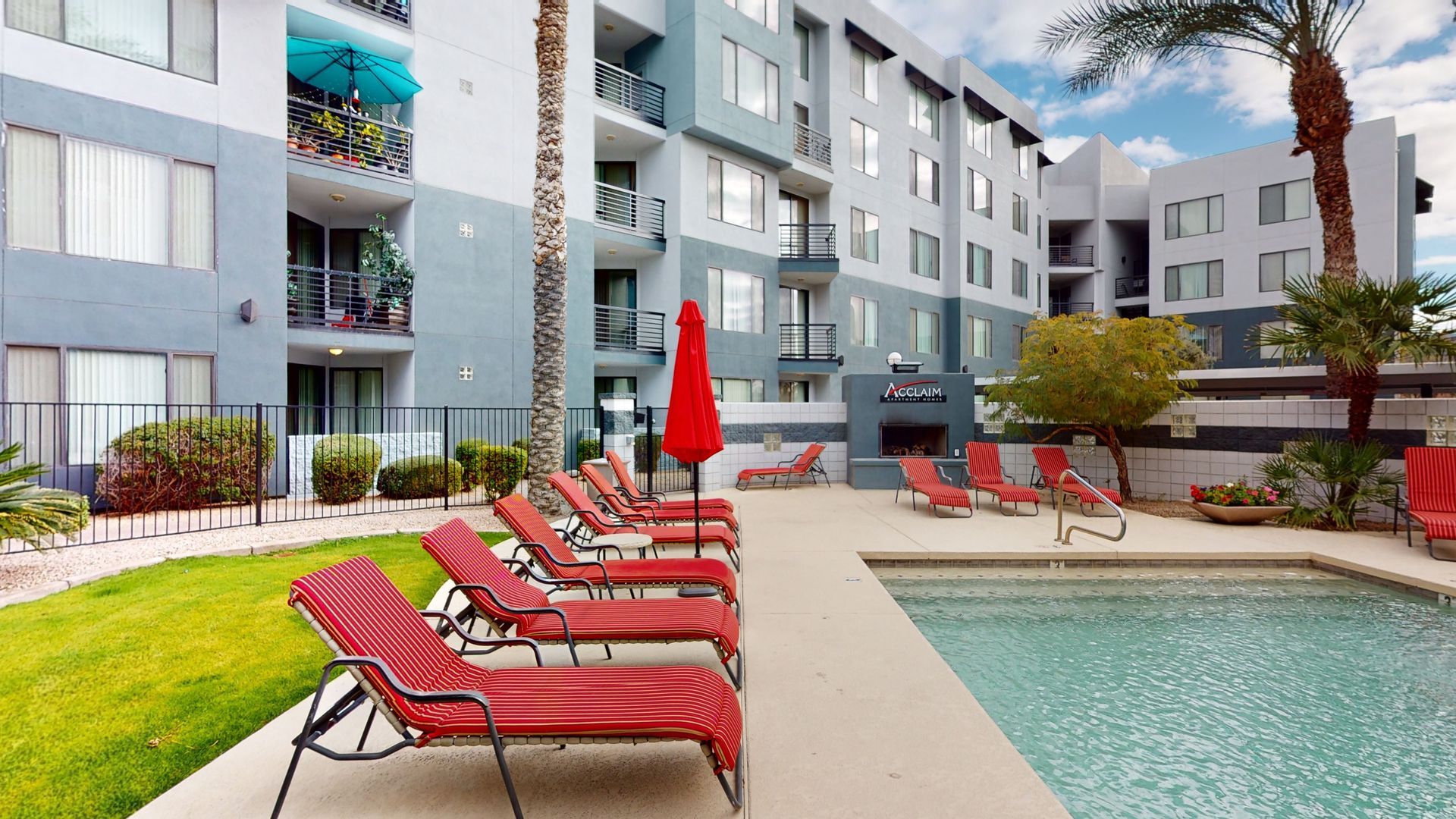 A large swimming pool surrounded by lounge chairs and umbrellas in front of a building.