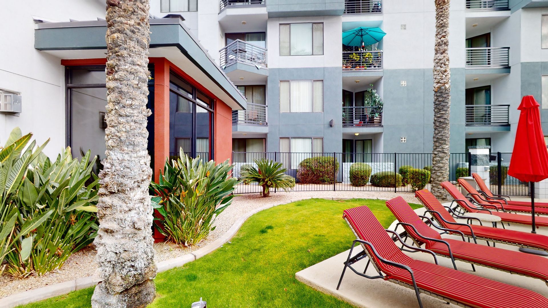 A row of red lounge chairs and umbrellas in front of a building.