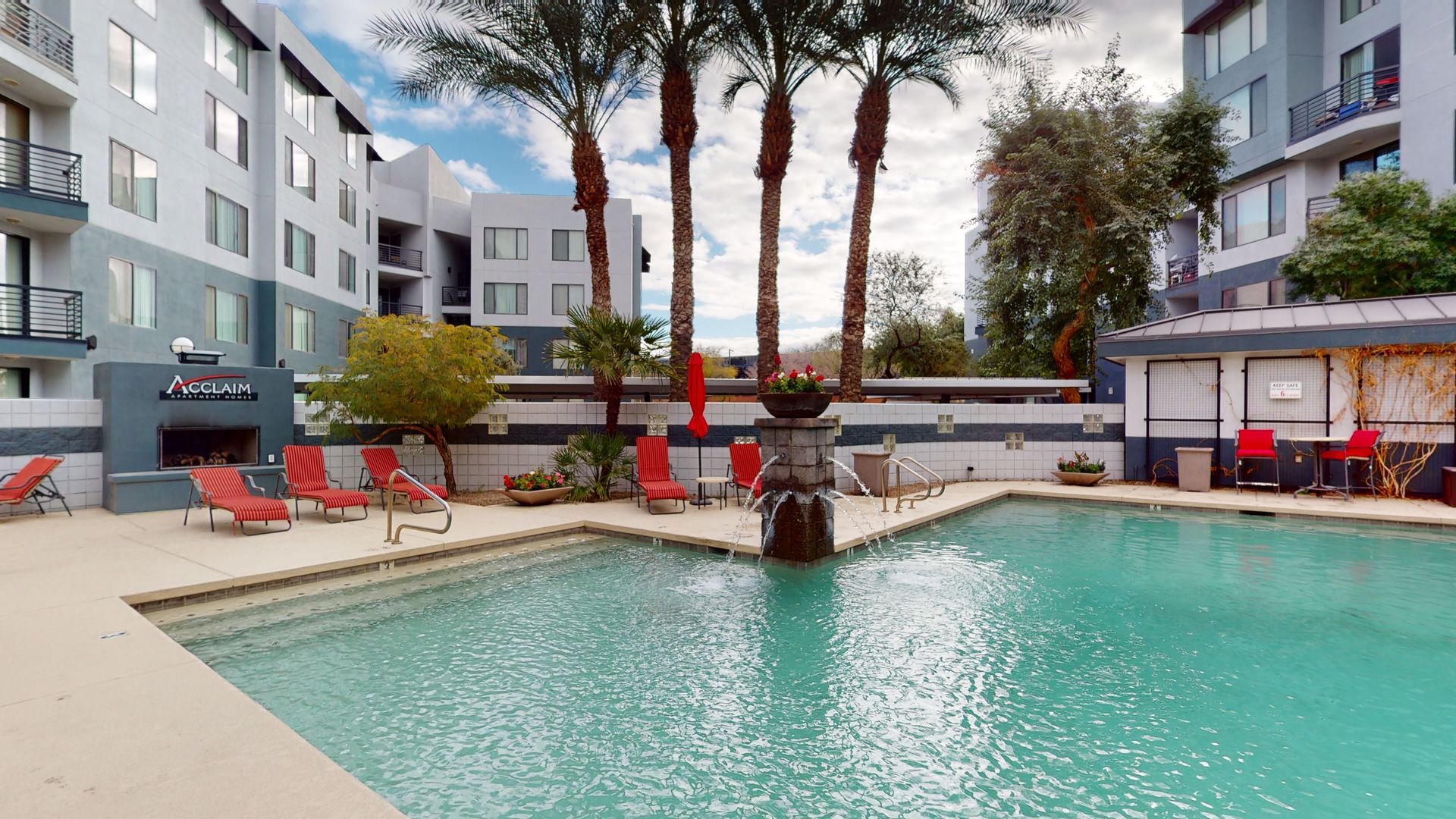A large swimming pool surrounded by chairs and palm trees in front of a building.