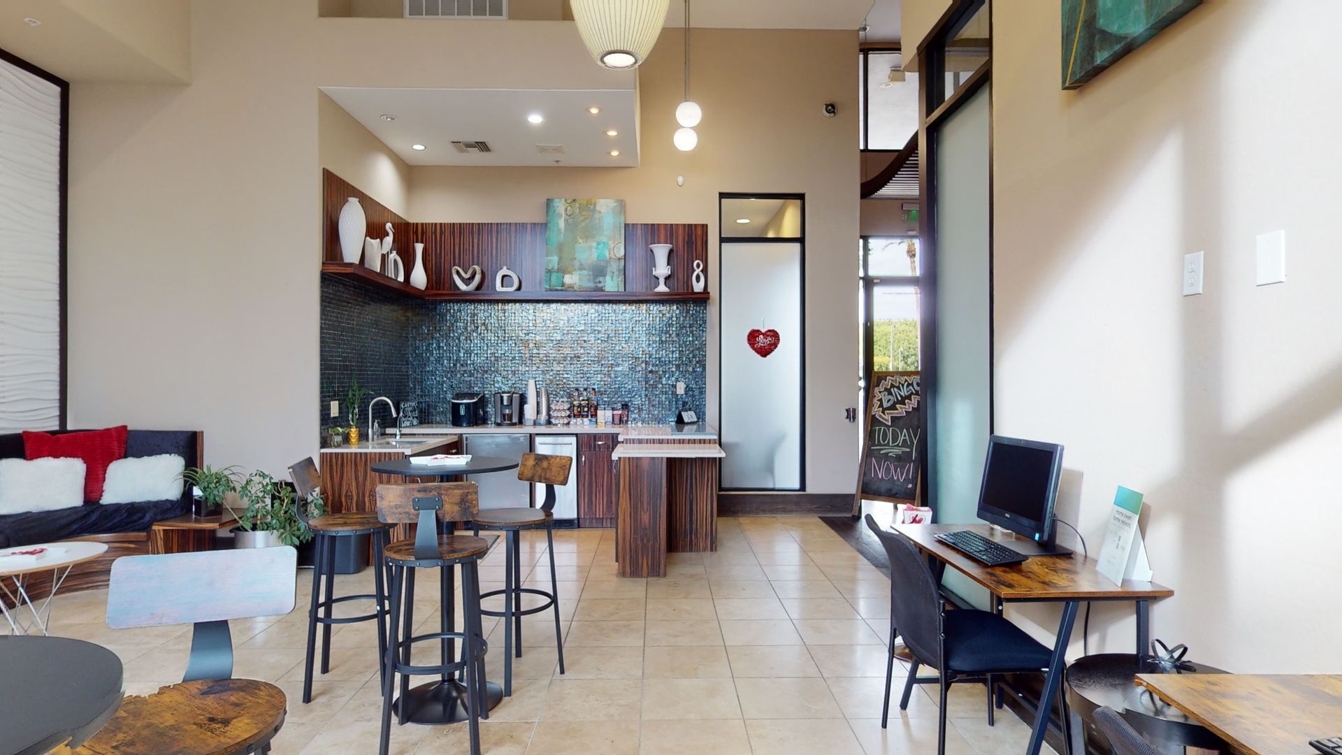 A living room with tables and chairs and a kitchen in the background.