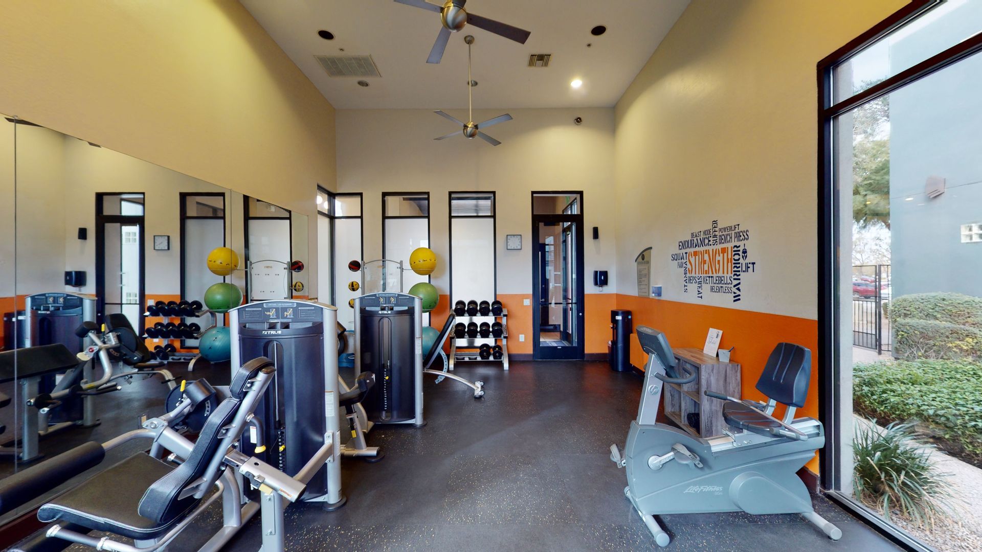 A gym with a lot of equipment and a ceiling fan