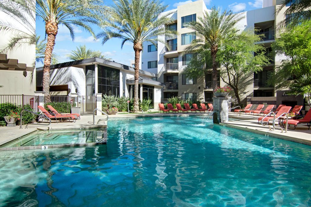 A large swimming pool surrounded by palm trees and chairs in front of a building.