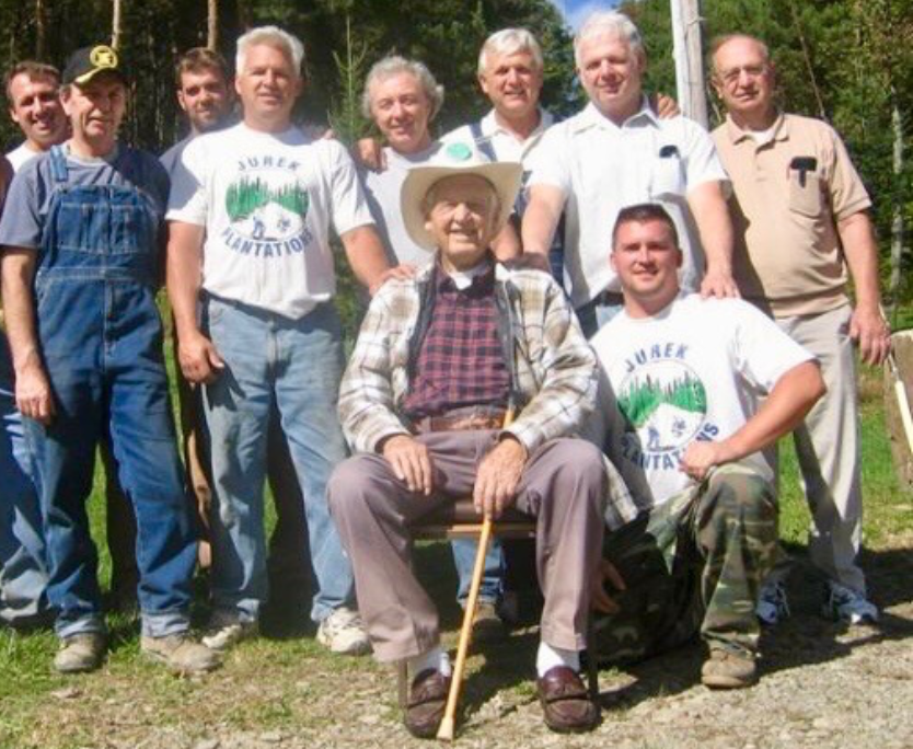 A group of ten people stand or sit together outdoors on a sunny day, wearing casual clothing, including "Jurek" t-shirts.