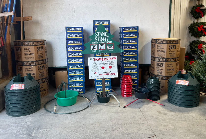 A display of Christmas tree stands and related accessories, including stacked boxes, green plastic bases, and signage.