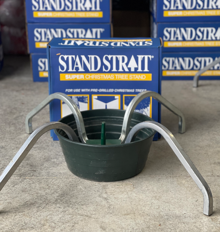 A Stand Strait super Christmas tree stand with a green basin and four metal legs, positioned in front of its product box.