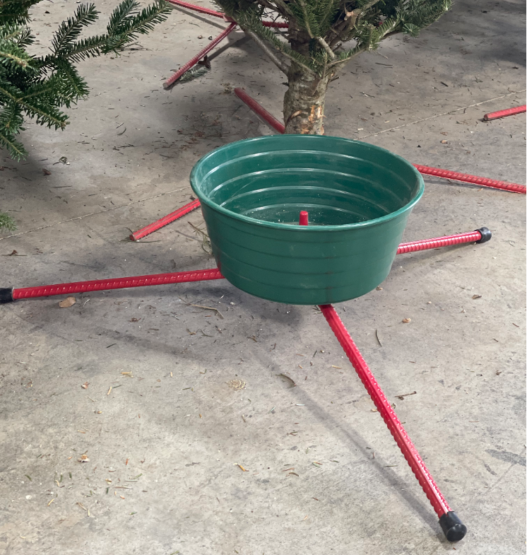 A green plastic Christmas tree stand with red metal legs sitting on a concrete floor.