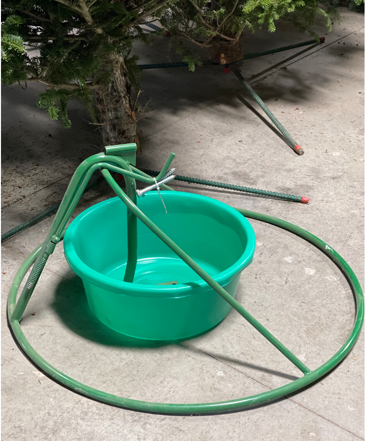 A green metal Christmas tree stand with a central plastic water basin sitting on a concrete floor.