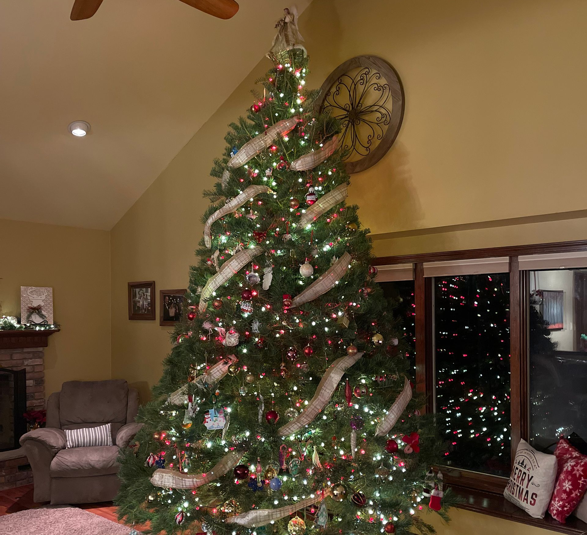 Christmas tree decorated with lights, ornaments, and ribbon, surrounded by presents in a warmly lit living room.