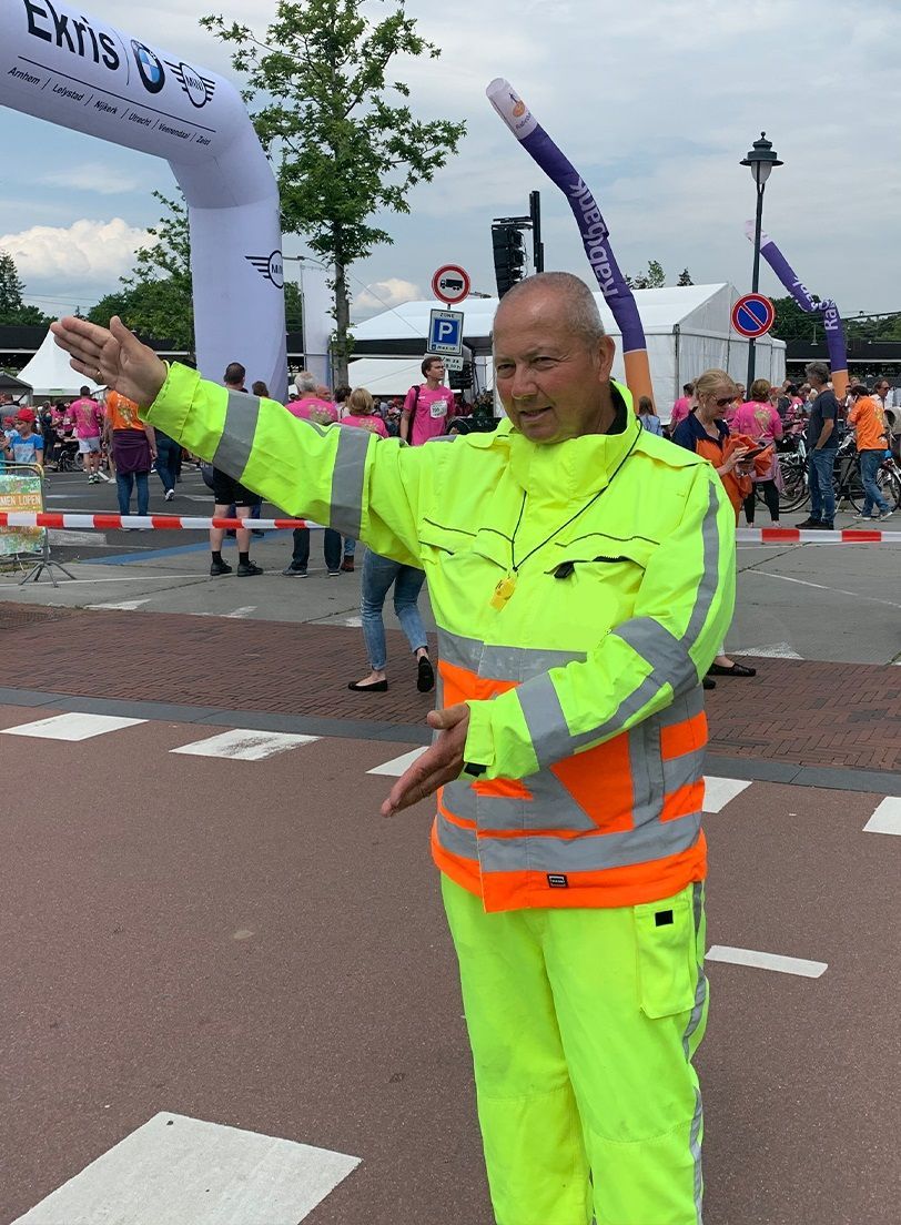 Een man in een neongeel jasje staat voor een uitgangsbord